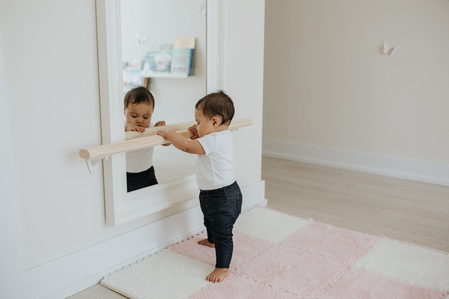 6 month old baby girl standing holding onto bar and looking in mirror - Barrie Lifestyle Photography