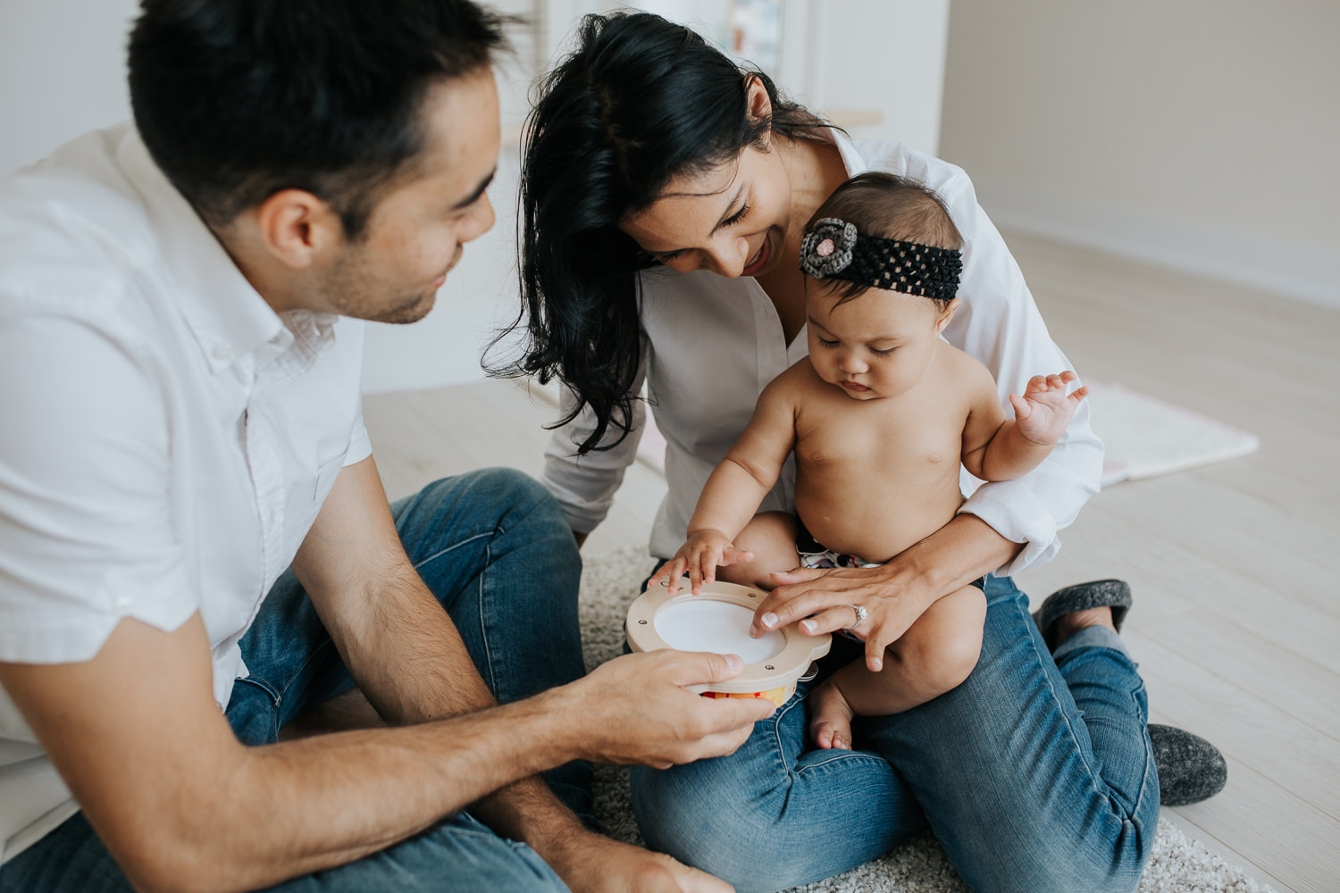 parents sitting on nursery floor with 6 month old baby daughter playing with toy drum - Barrie In-Home Photography