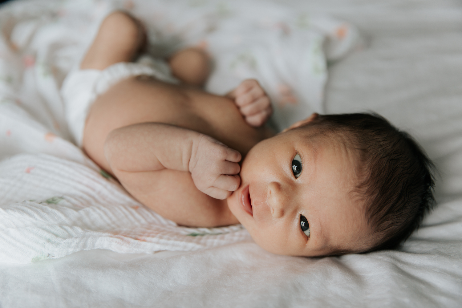 2 week old baby girl in diaper lying on bed, looking at camera - Markham In-Home Photos