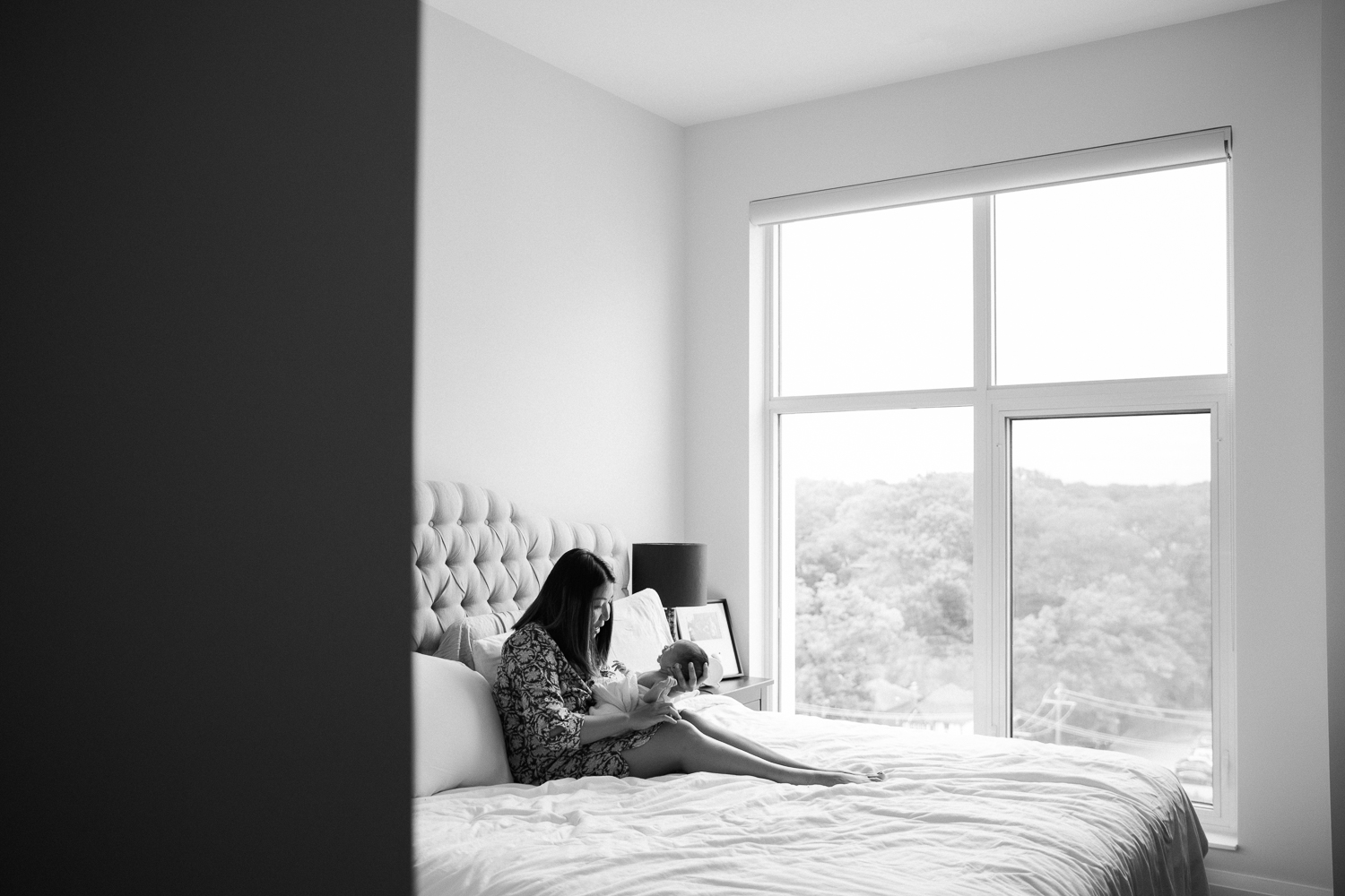 new mom sitting on bed holding swaddled 2 week old baby girl - Barrie Lifestyle Photos