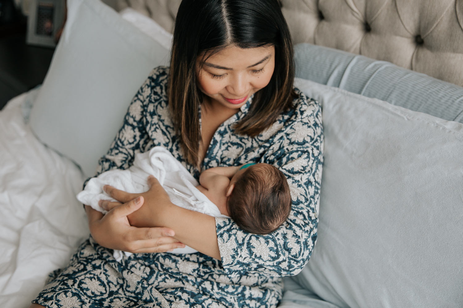 new mother sitting on bed holding swaddled 2 week old baby daughter - Newmarket Lifestyle Photography