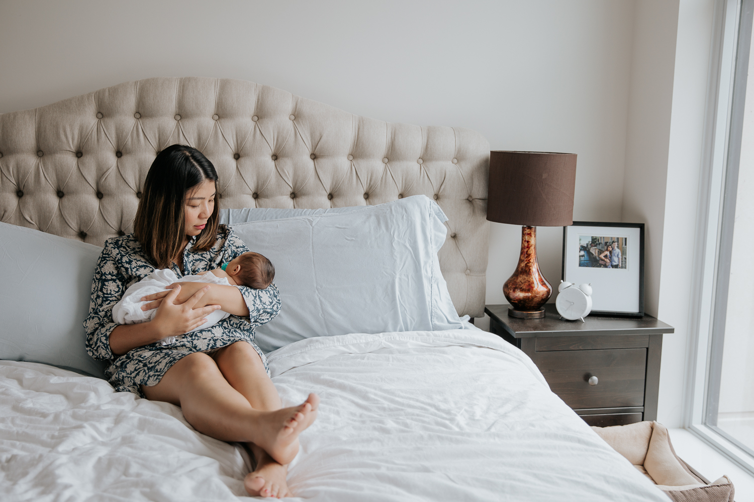 new mom sitting on bed holding swaddled 2 week old baby girl - Stouffville Lifestyle Photos