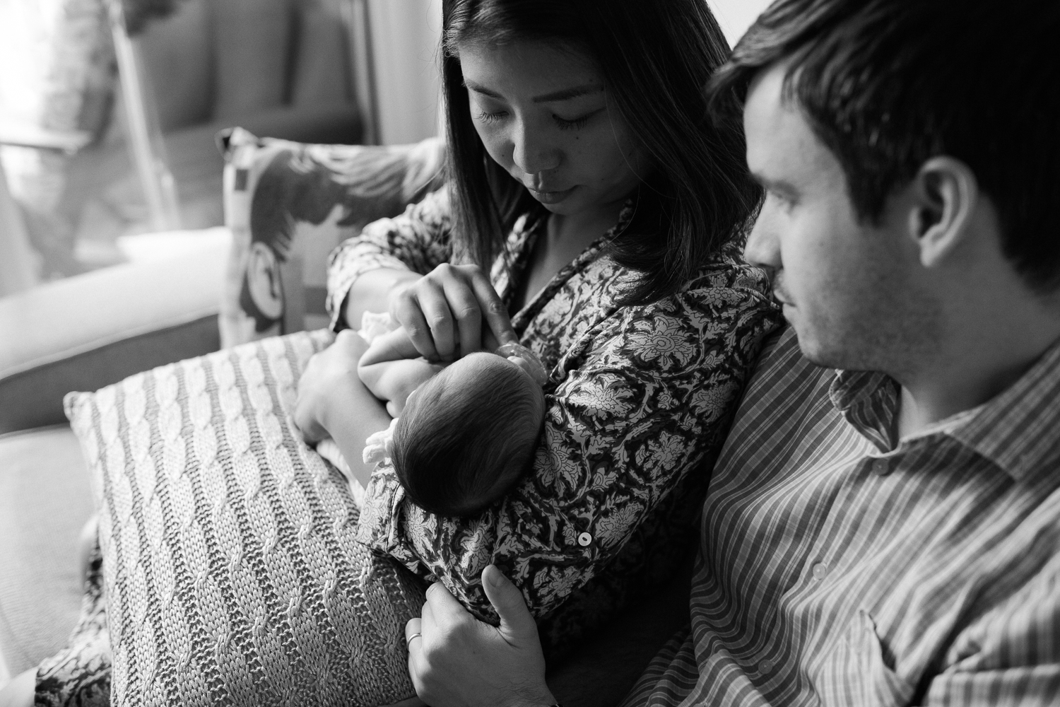 first time parents sitting on couch holding sleeping 2 week old baby girl - Newmarket Lifestyle Photos