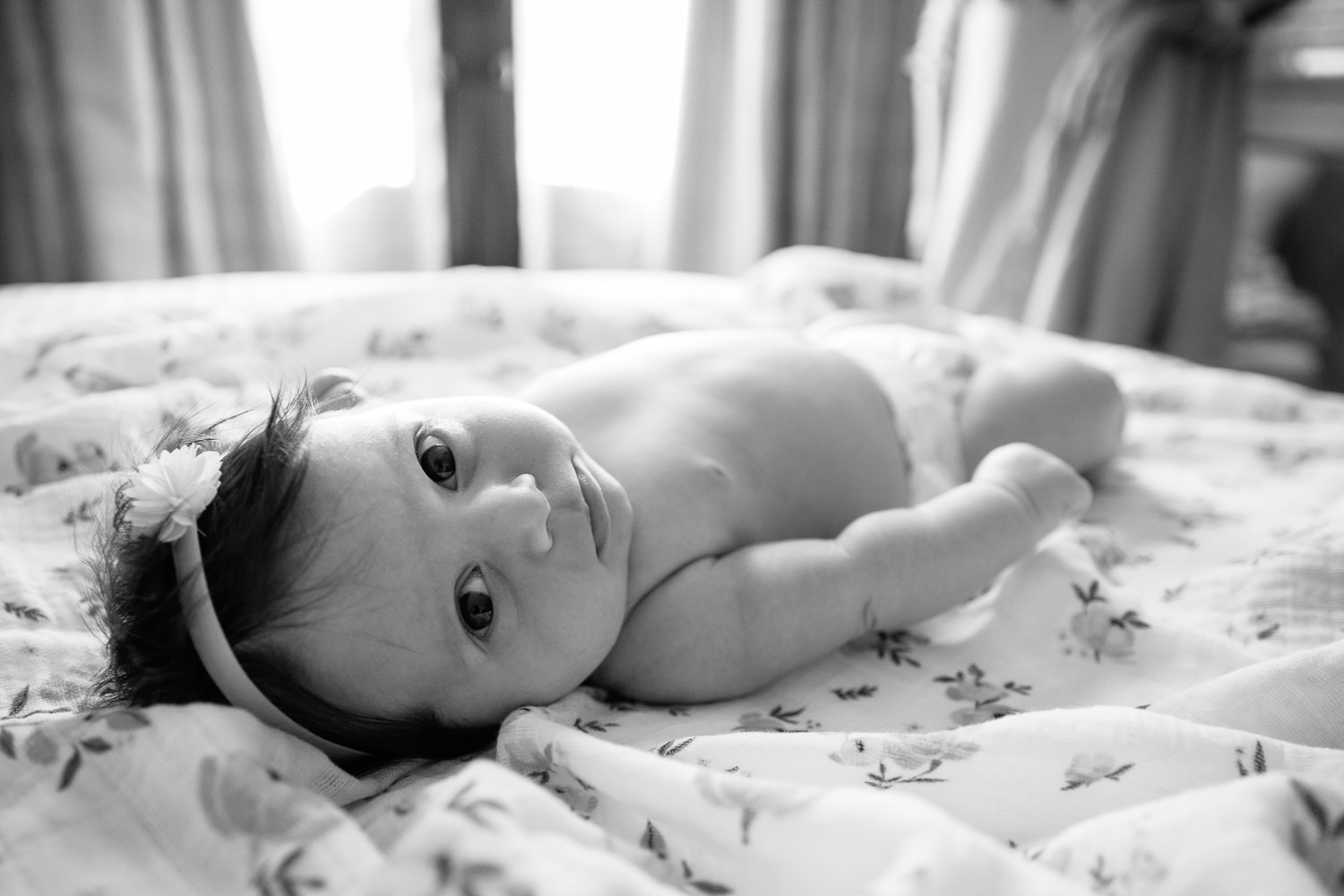 2 month old baby girl in diaper with lots of dark brown hair wearing headband lying on yellow floral blanket, looking at camera - GTA Lifestyle Photos