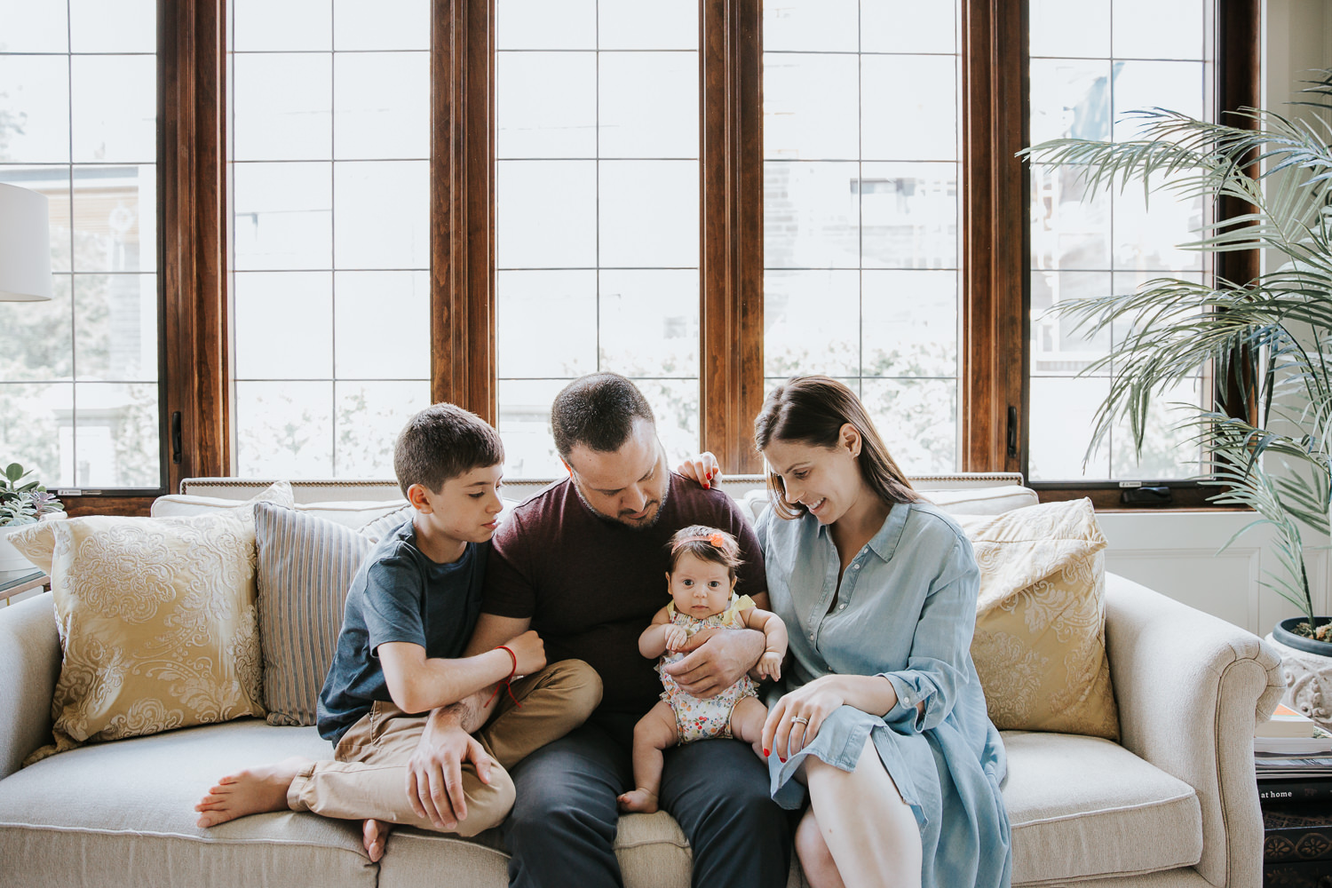 family of four sitting on couch, mom, dad and 9 year old son looking at 2 month old baby daughter in father's lap - Stouffville Lifestyle Photos