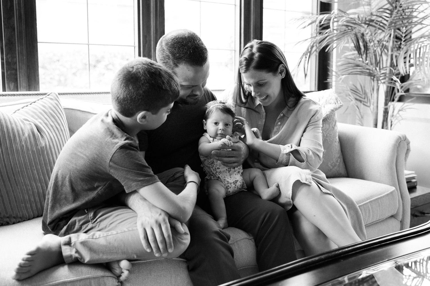 family of four sitting on couch, mom, dad and 9 year old son looking at 2 month old baby daughter in father's lap - Barrie Lifestyle Photos