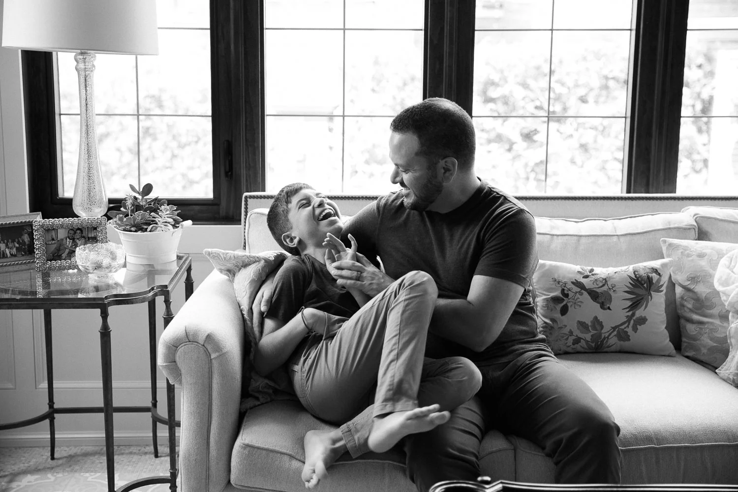 father hugs and tickles 9 year old son on couch, boy laughs - Markham Lifestyle Photography