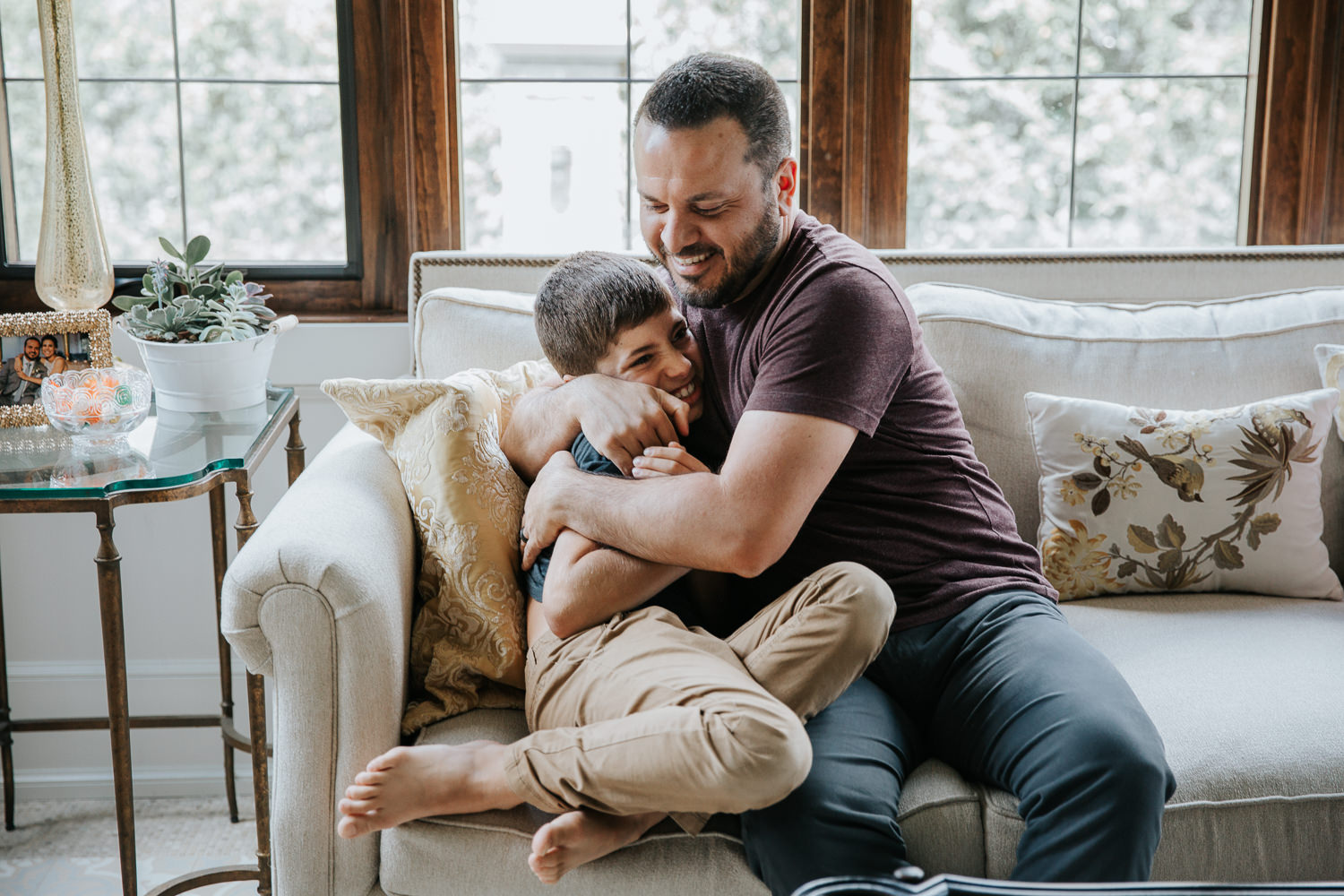 father hugs and tickles 9 year old son on couch, boy laughs - Stouffville Lifestyle Photography