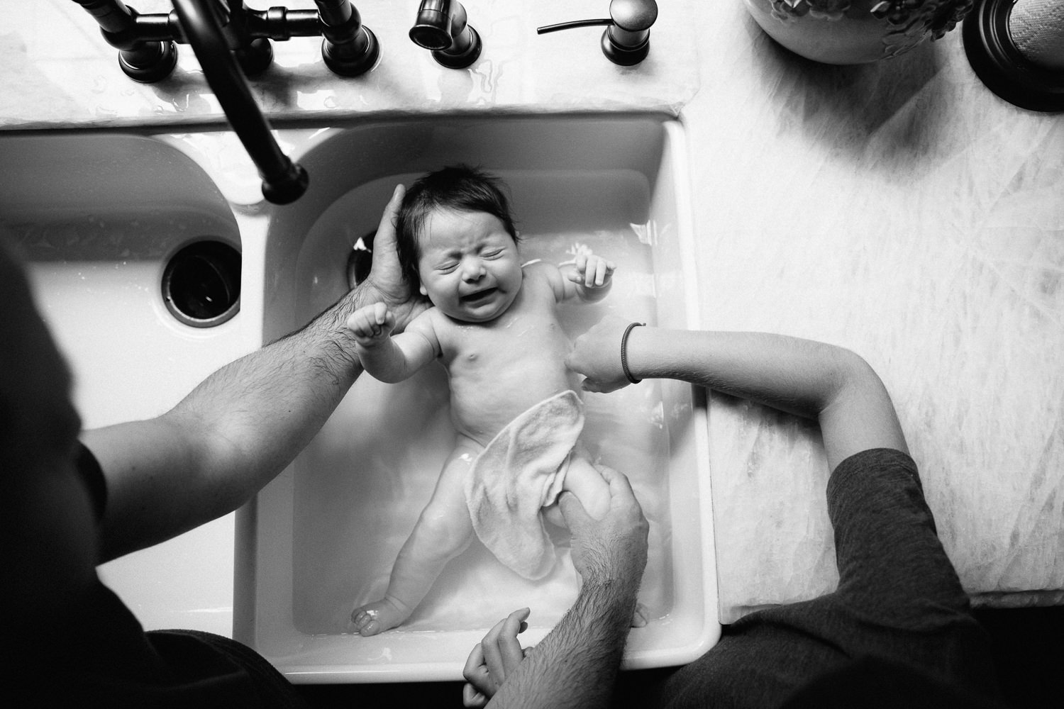 2 month old baby girl with lots of dark brown hair in kitchen sink getting a bath from dad and 9 year old big brother - GTA In-Home Photography