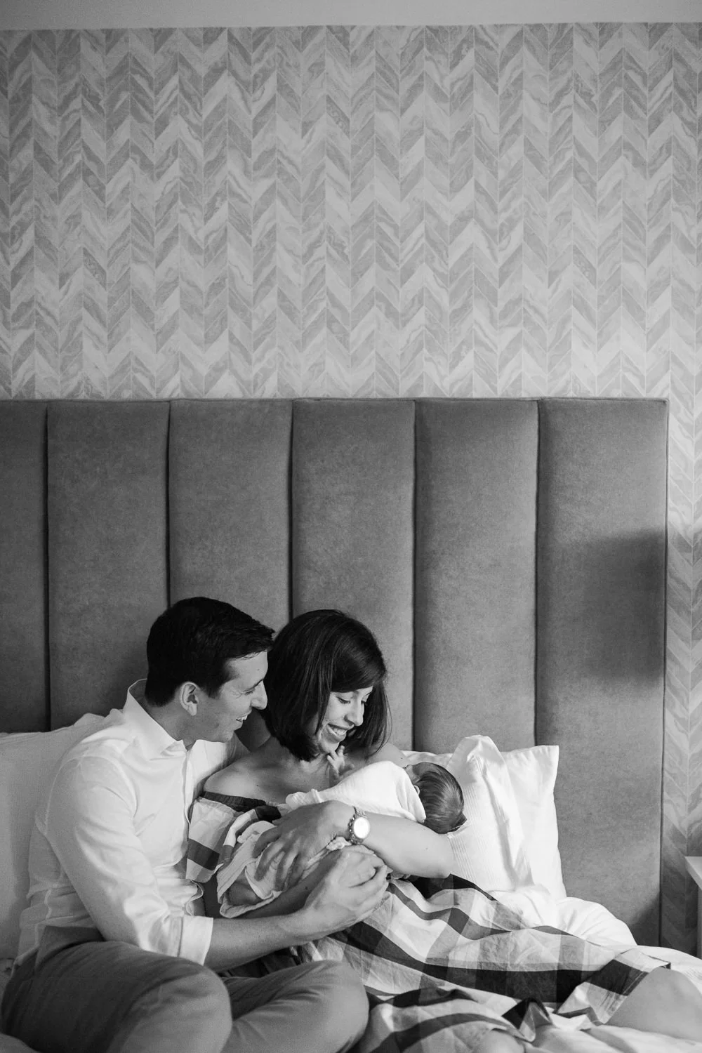 new parents sitting on master bed, mom holding 2 week old baby boy with dad sitting next to them - Barrie In-Home Photos