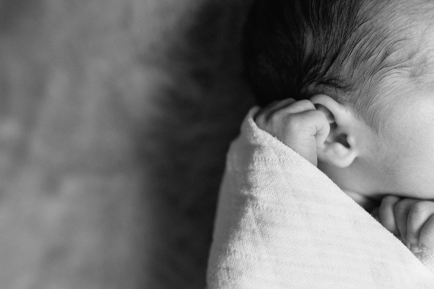 2 week old baby boy with dark hair lying on fur blanket in white swaddle, close up of hand and ear - GTA Lifestyle Photos