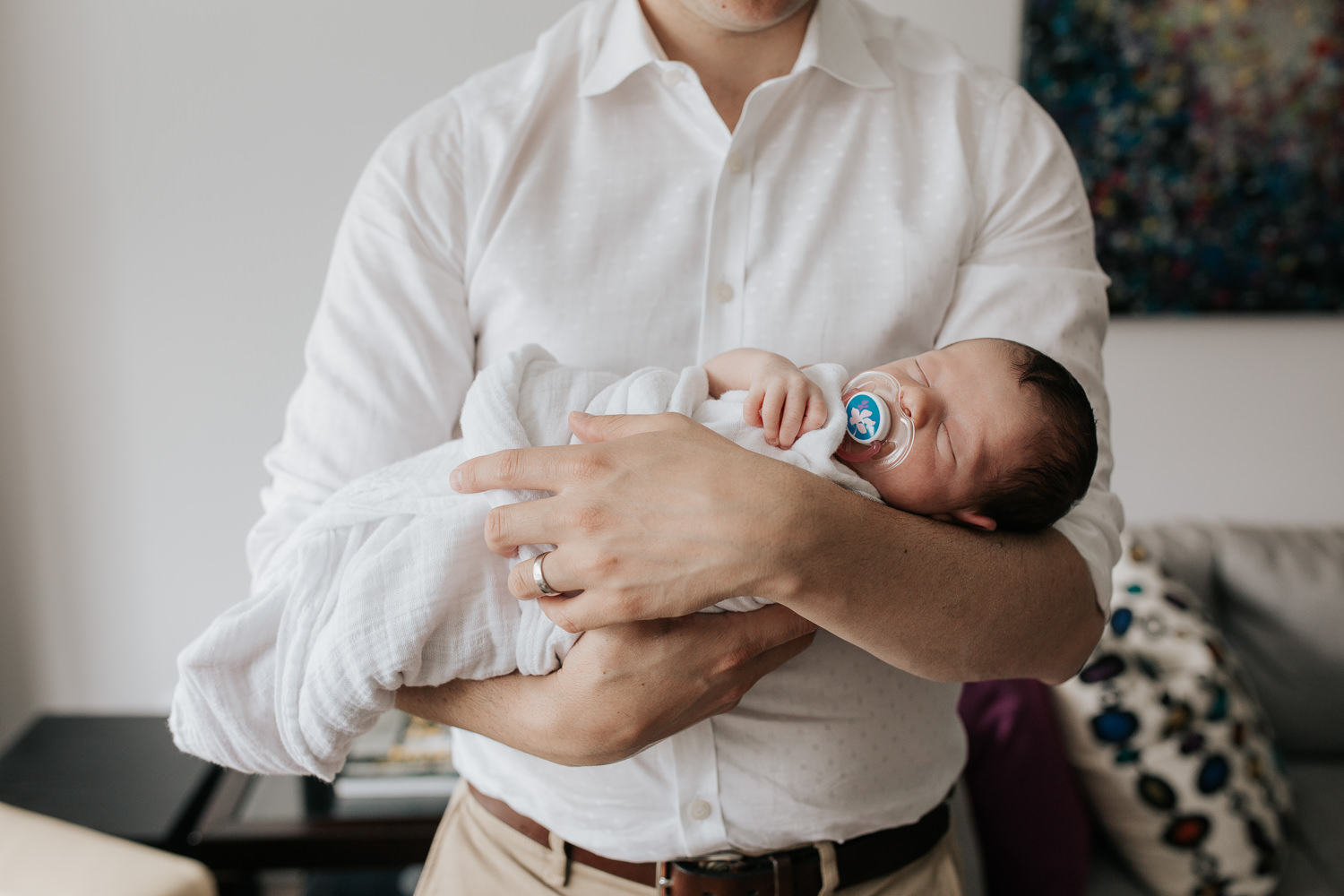 new father standing in living room holding sleeping 2 week old baby boy in white swaddle - 