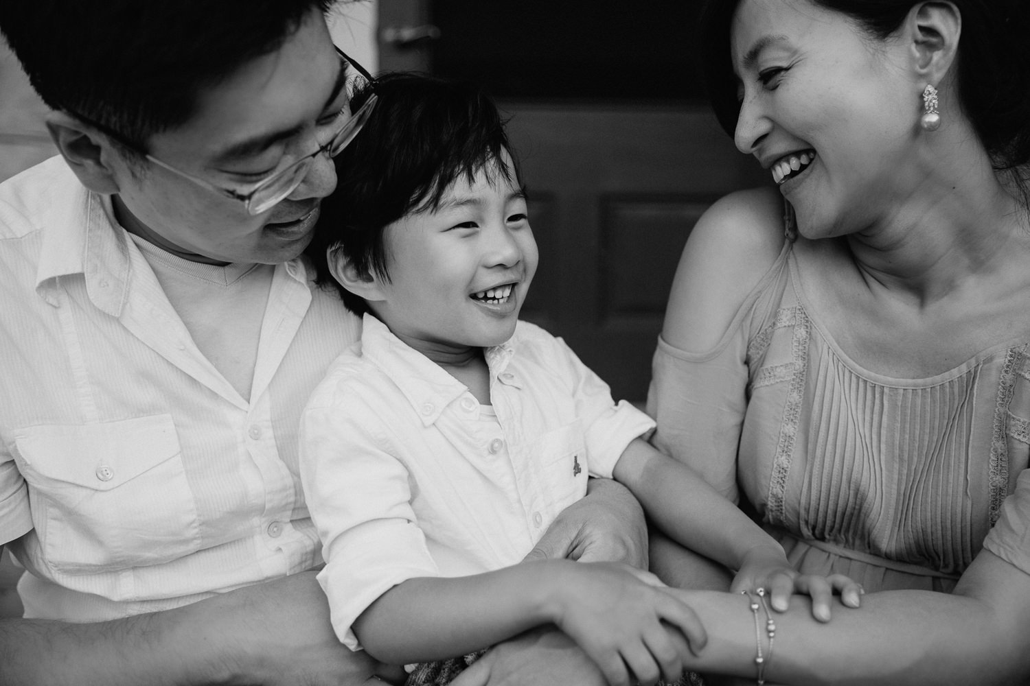 family of 3 sitting on front porch, toddler son sitting on dad's lap, mom and son smiling- Stouffville Lifestyle Photography