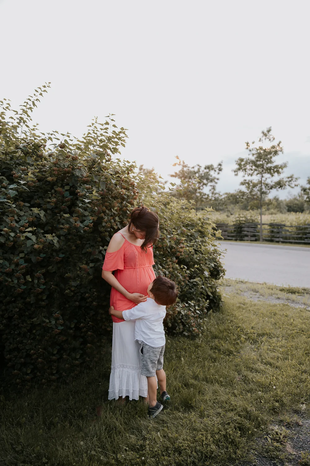 3 year old toddler boy hugging his 7 month pregnant mom's legs on his tip toes, mother holding baby bump and looking down at son - GTA In-Home Photos