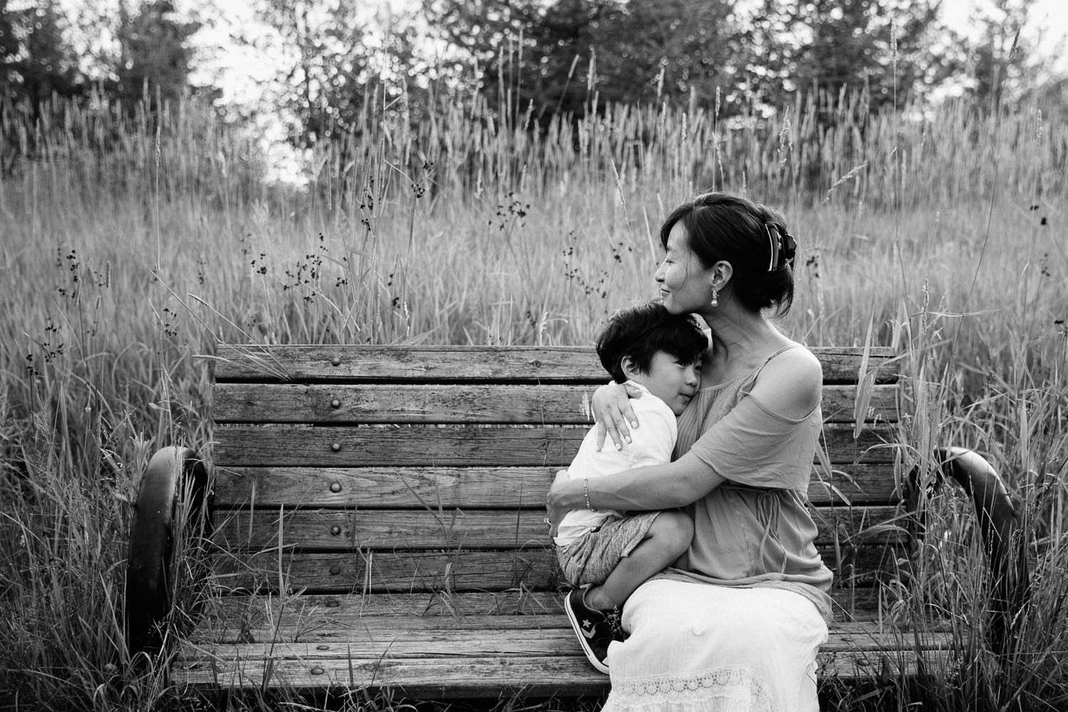 3 year old toddler boy cuddles up against mom on bench as she snuggles him to her chest - GTA In-Home Photography