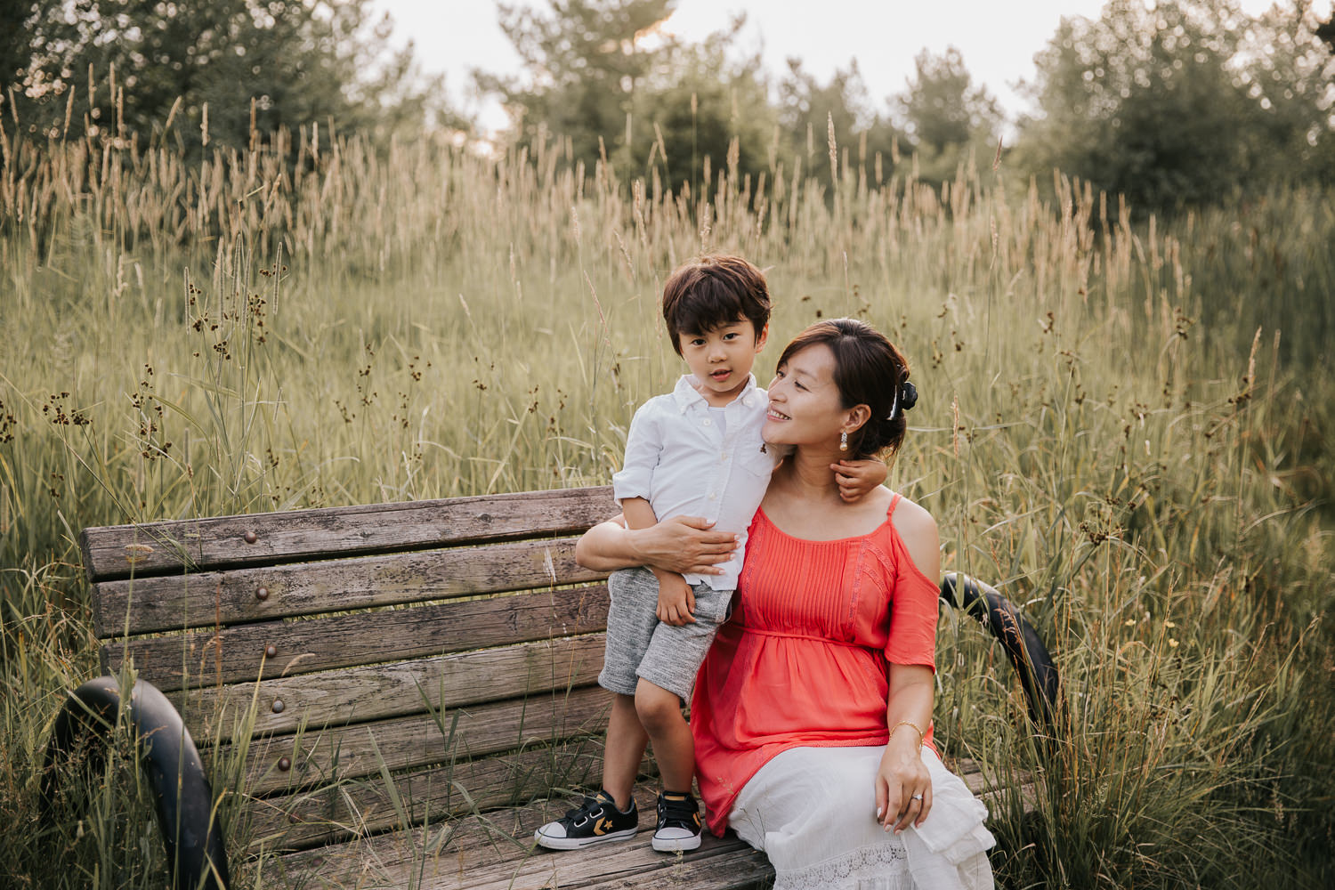 3 year old toddler boy standing on park bench leaning on mother with arm around her neck, mom looking and smiling at son - Newmarket In-Home Photos