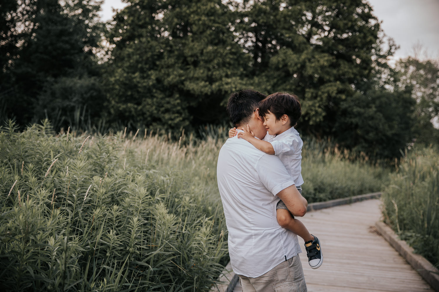 3 year old toddler boy being carried down boardwalk by dad, his arms around father's neck - Stouffville In-Home Photos