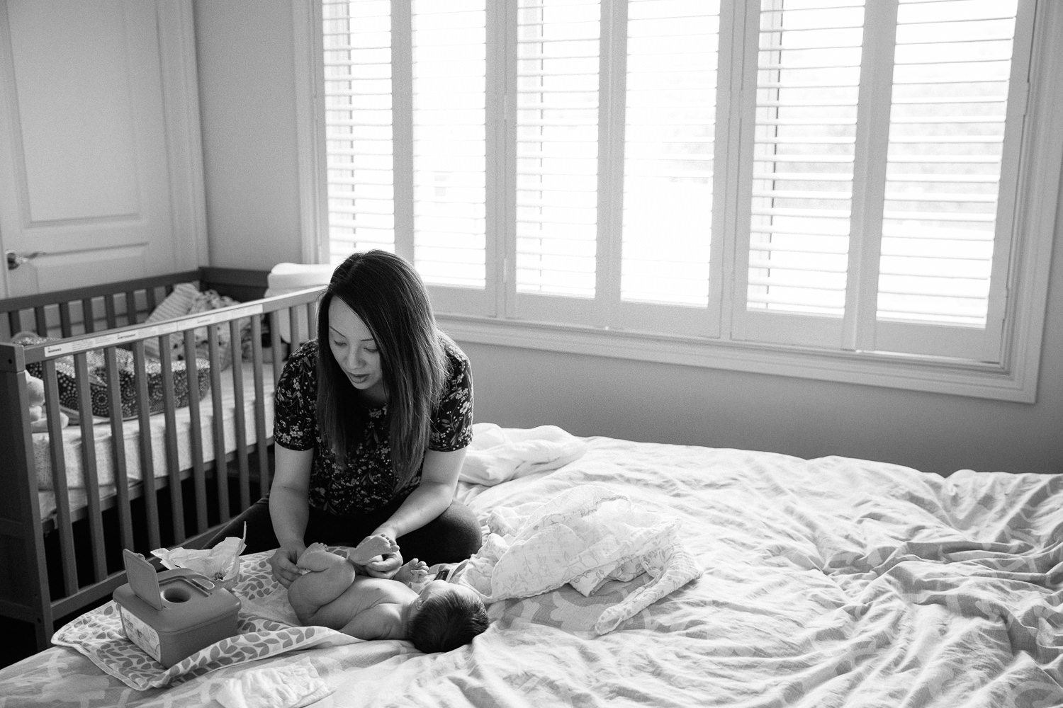 mom with long dark hair sitting on edge of master bed changing 2 week old baby girl's diaper - Newmarket In-Home Photos