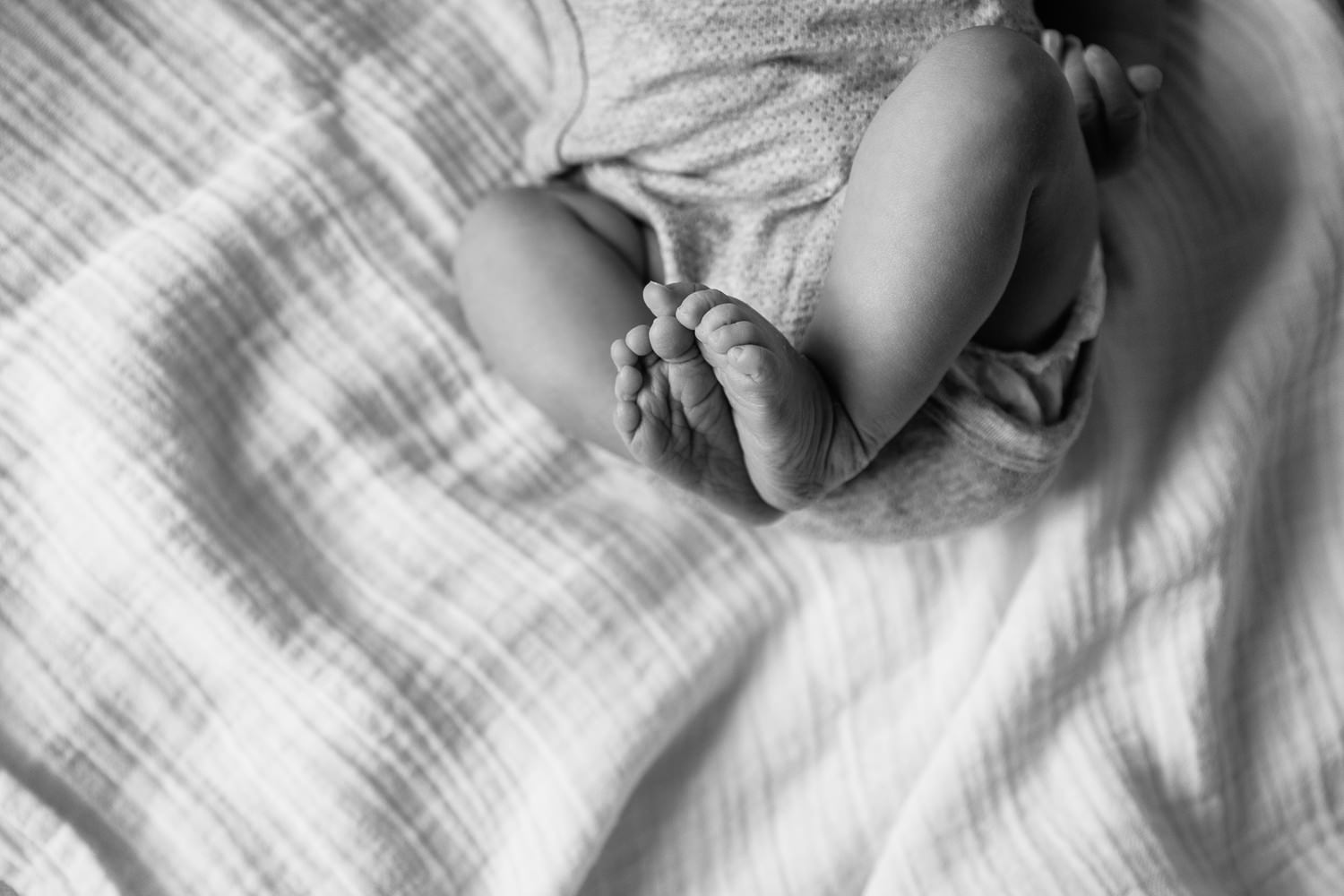 2 week old baby girl in onesie lying on bed, close up of feet  - Barrie In-Home Photography