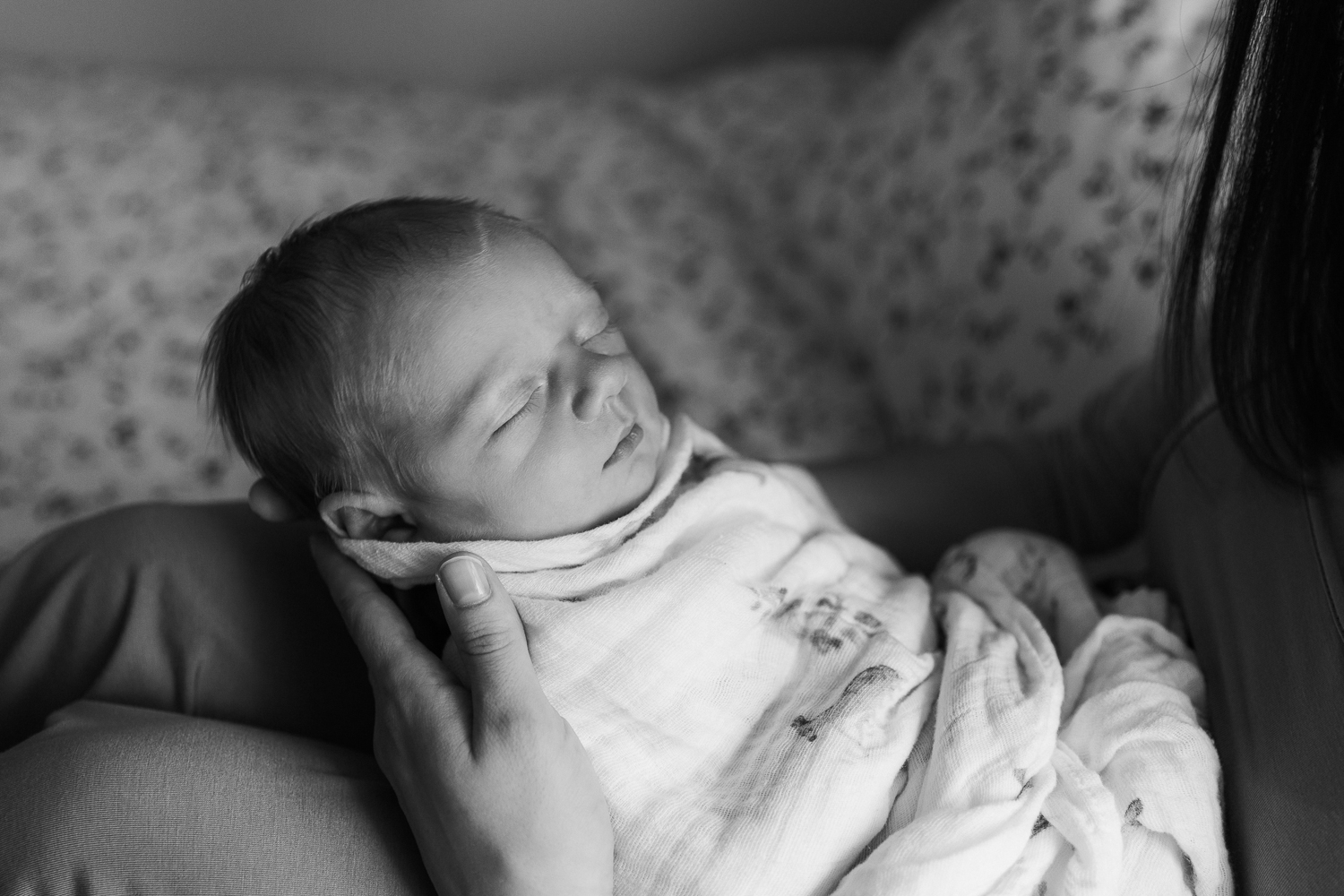 3 week old swaddled baby boy with red hair sleeping in mother's lap as she sits on bed - Barrie In-Home Photography