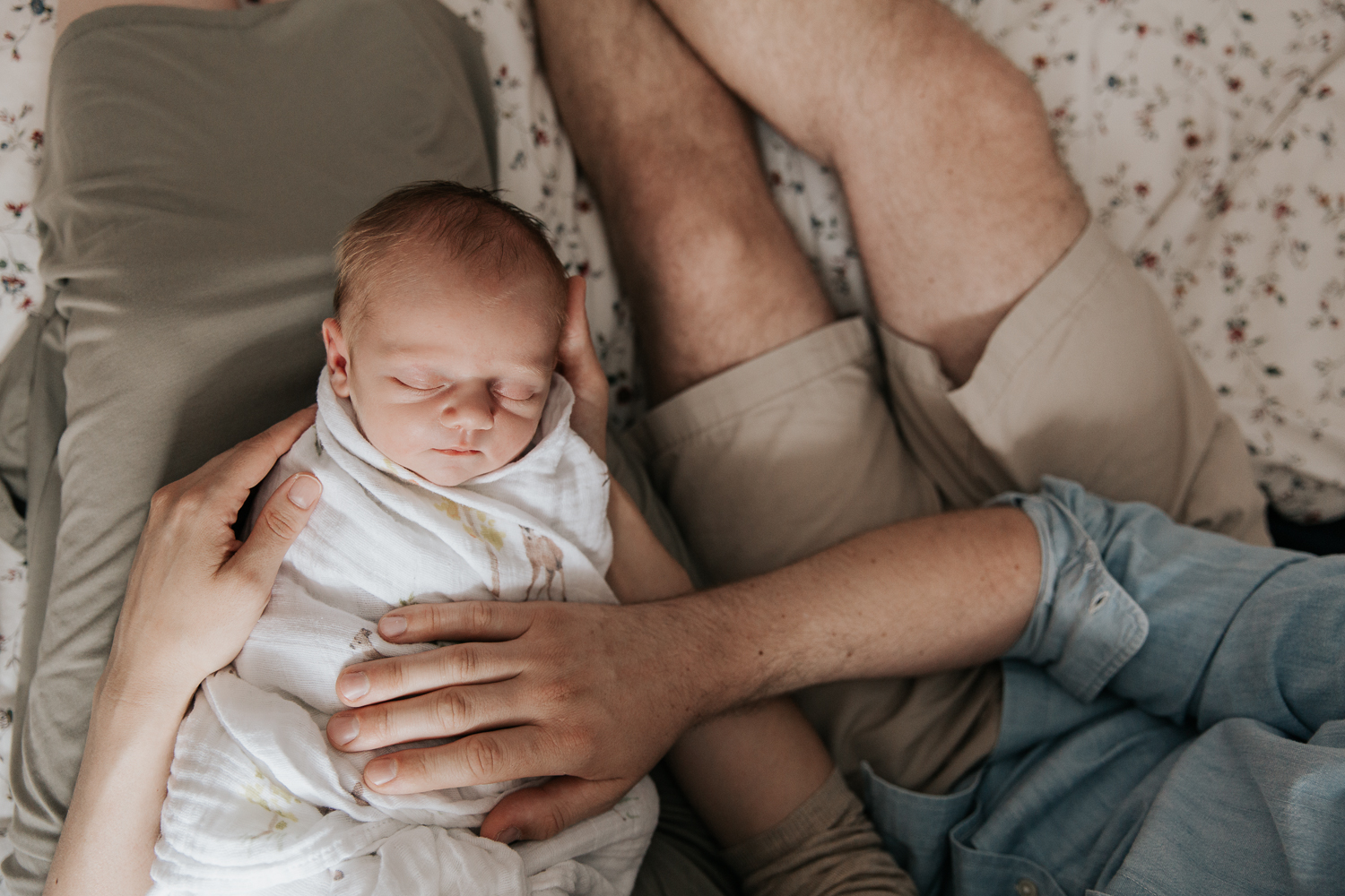 3 week old swaddled baby boy with red hair sleeping in mother's lap, dad sitting next them them with hand on son - Markham In-Home Photography