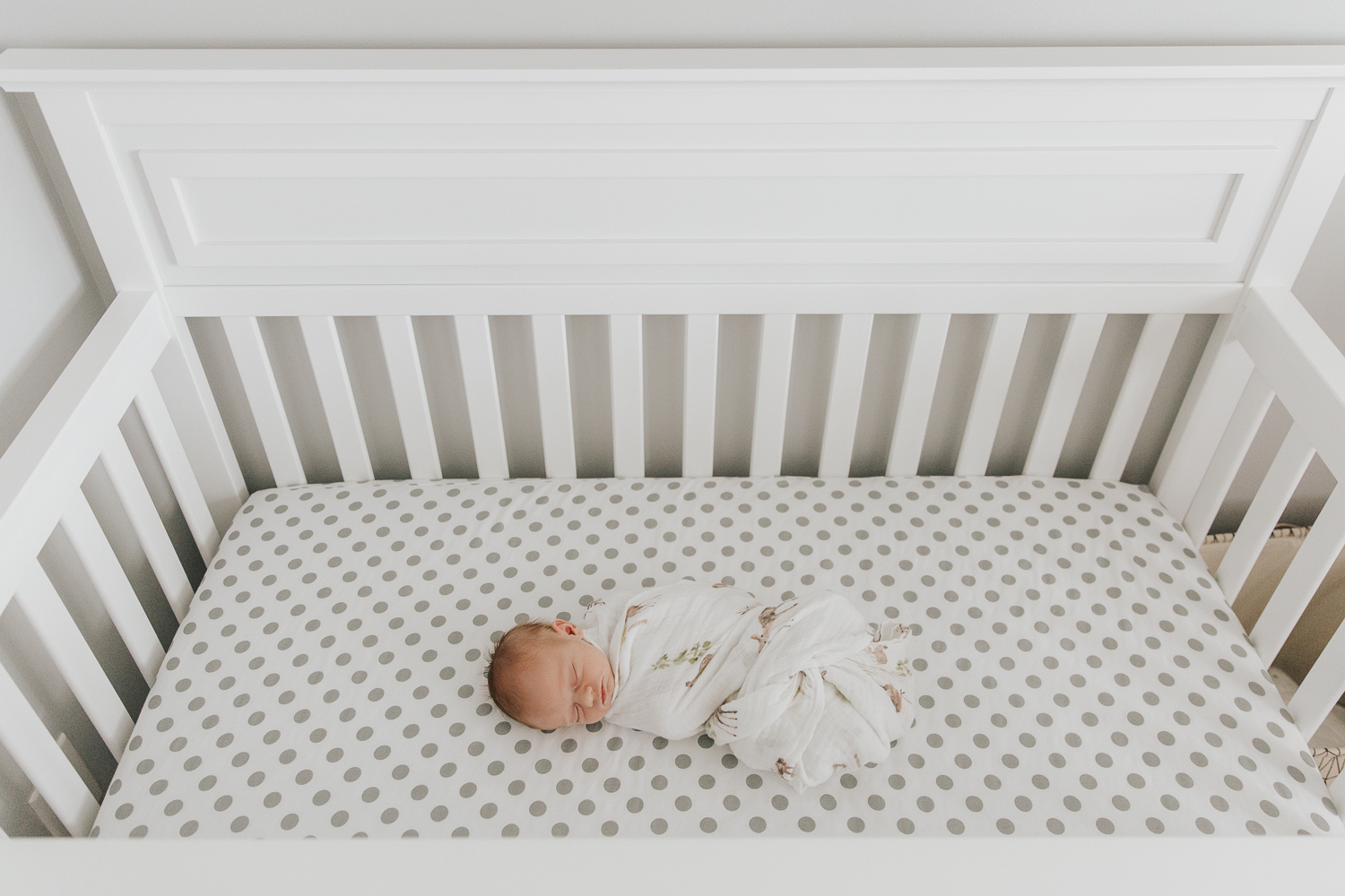 3 week old baby boy with red hair wrapped in swaddle and lying in crib with grey and white polka dot sheets, shot from above - Stouffville Lifestyle Photos