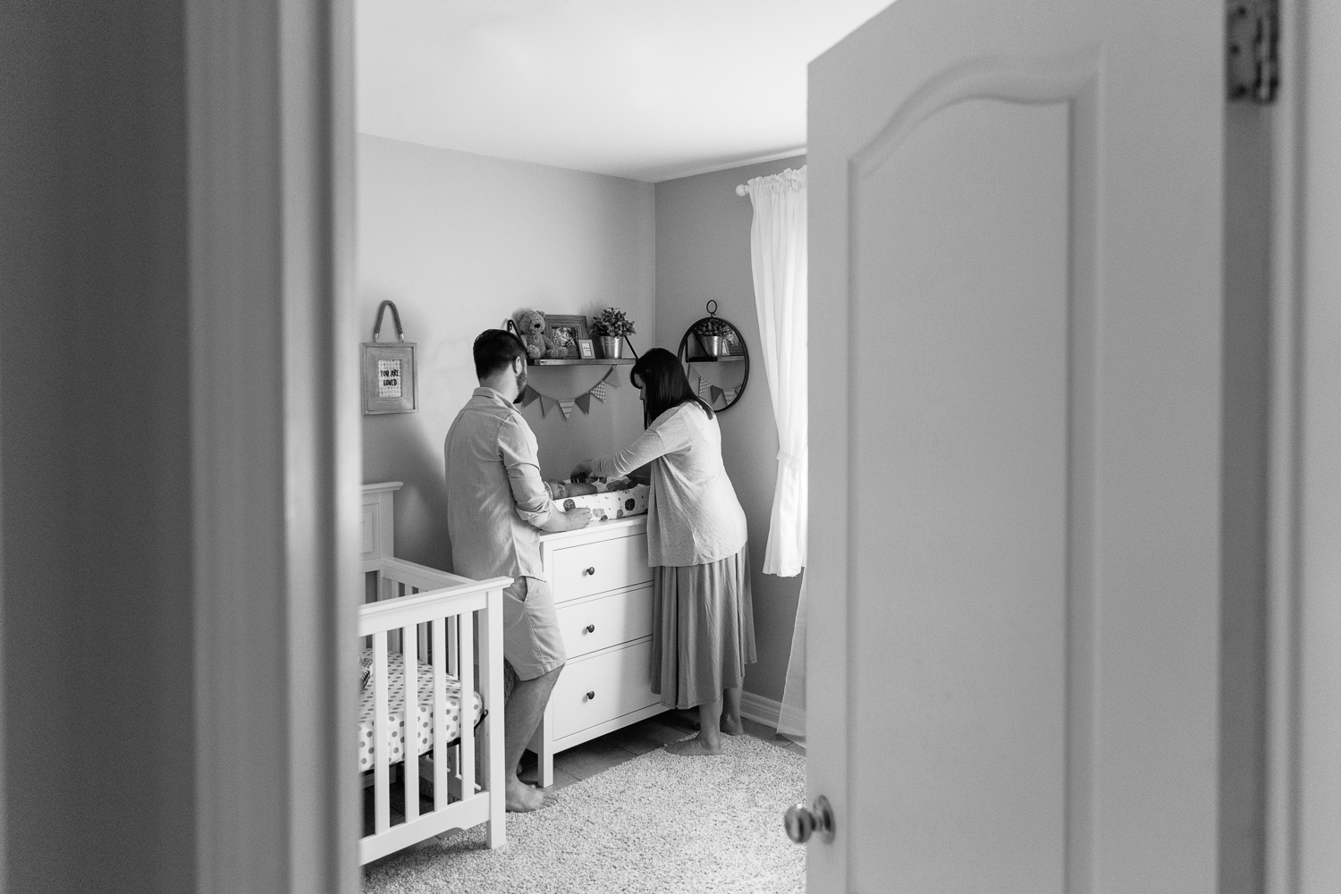 first time parents standing in nursery at change table putting new diaper on 3 week old baby boy - Newmarket Lifestyle Photography