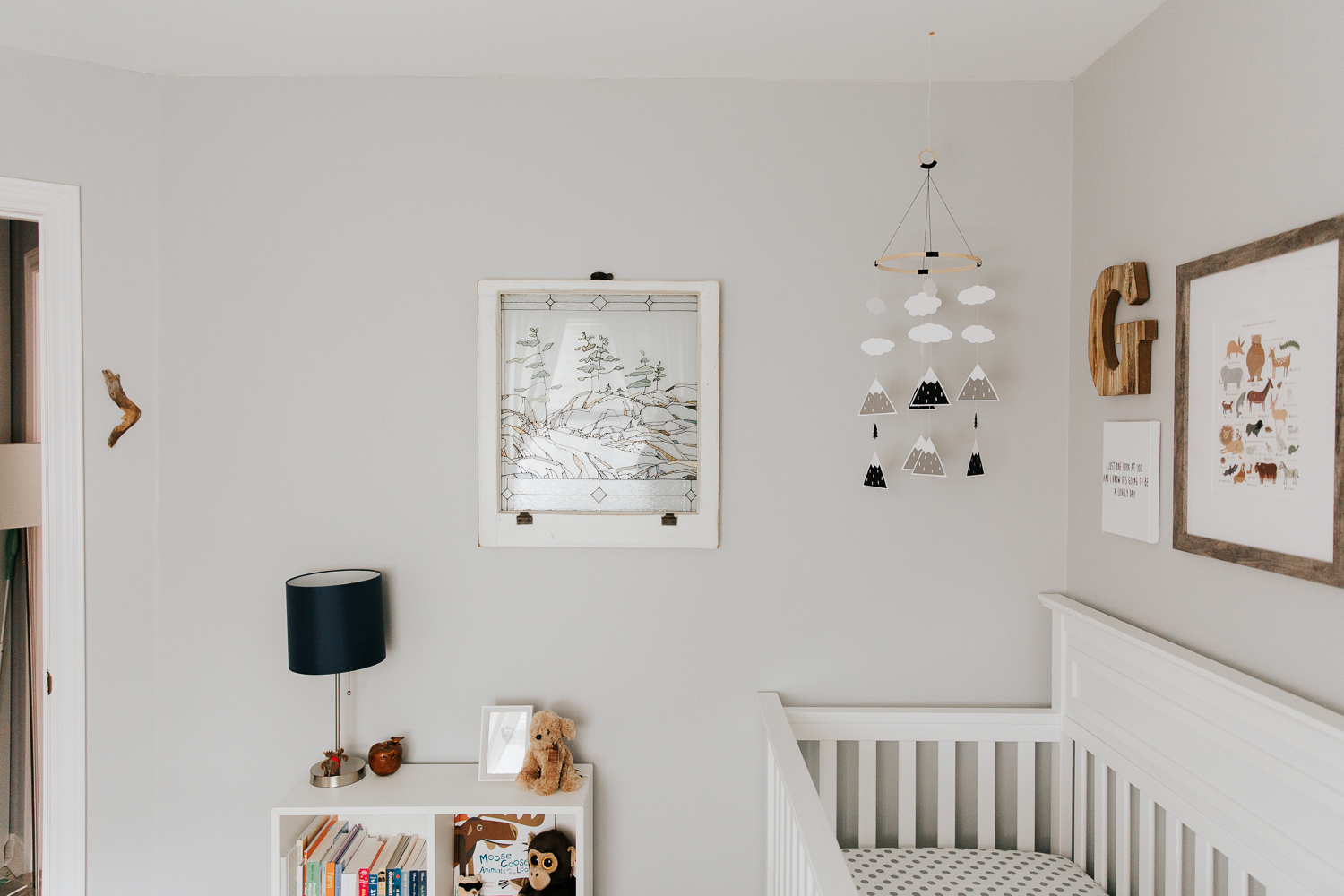 woodland nursery details, grey walls, white crib with a gallery wall, mountain mobile and stained glass window - Markham Lifestyle Photography