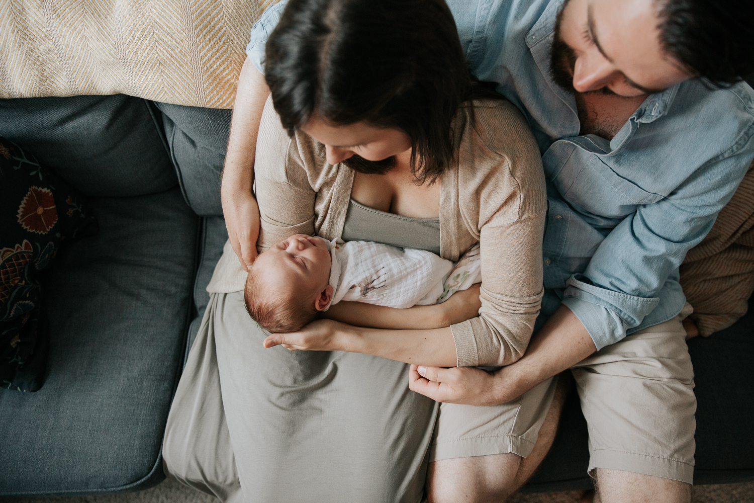 family of 3, new parents sitting on couch, mom holding 3 week old swaddled baby boy with red hair, dad with arm around mom looking at son - GTA Lifestyle Photos