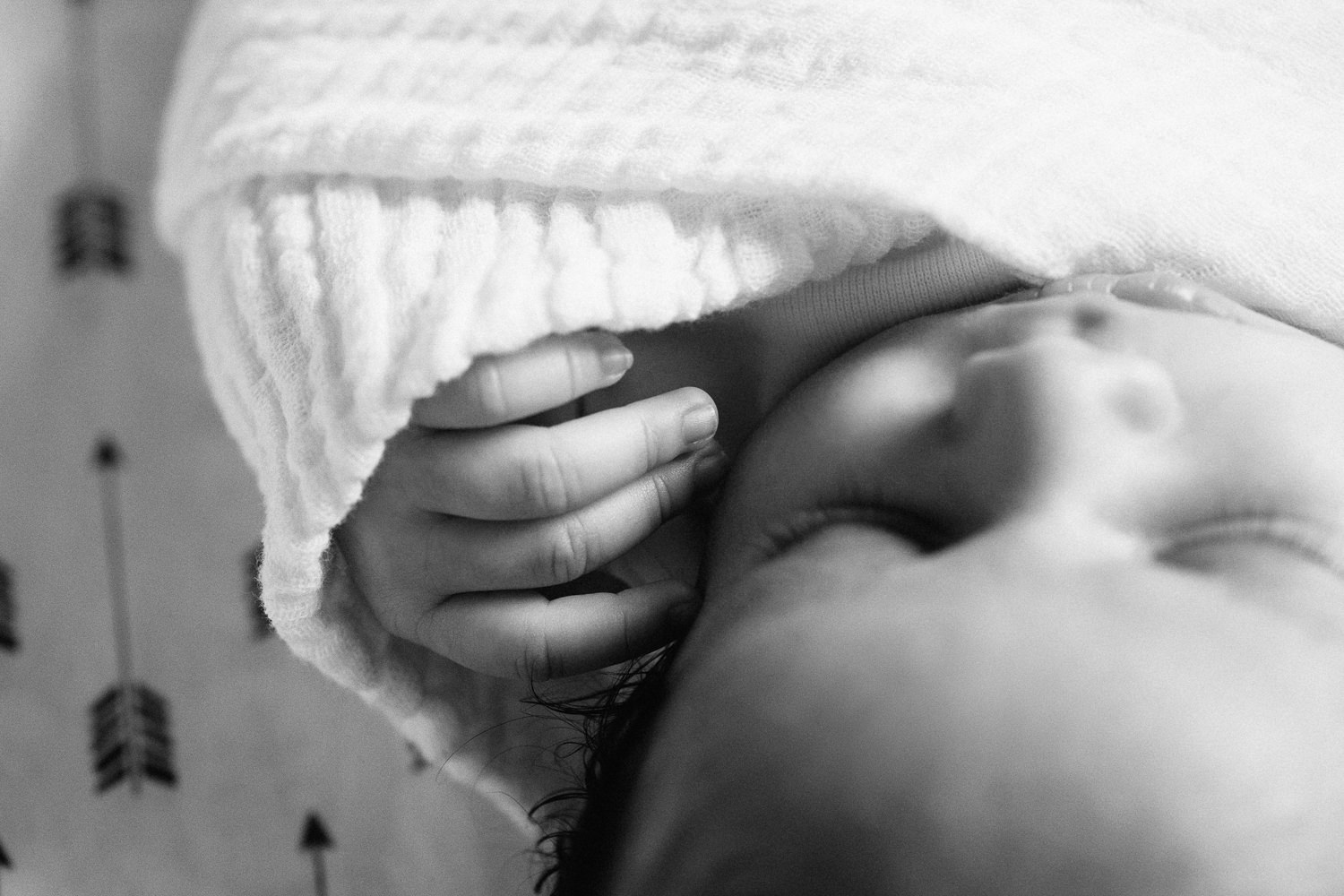 1 month old baby boy with dark hair wrapped in white swaddle lying asleep in crib on black and white arrow patterned sheet, close up of hand near face - Barrie Lifestyle Photography