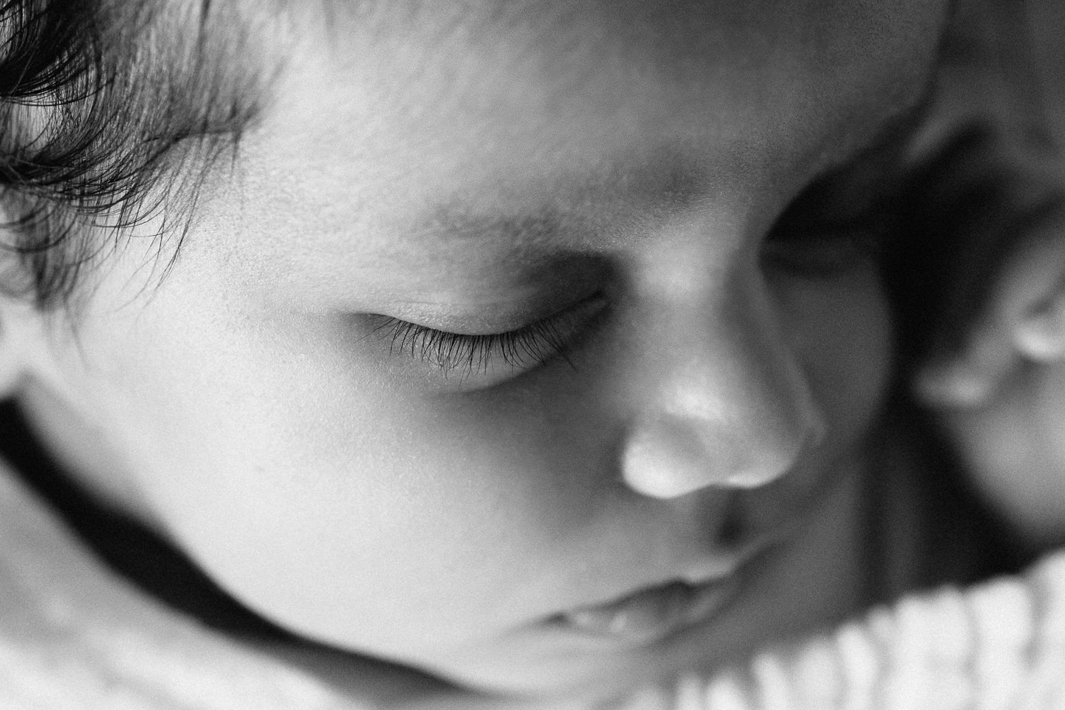 1 month old baby boy with dark hair wrapped in white swaddle lying asleep. head tilted to one side, close up of eyelashes - Newmarket In-Home Photography