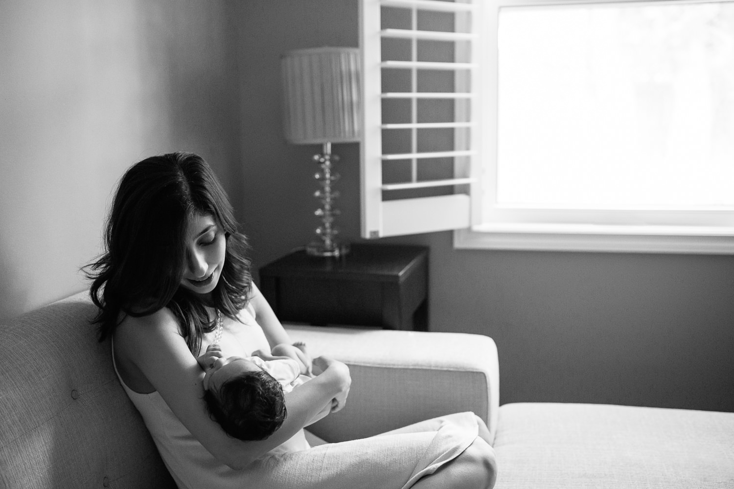 new mom sitting on couch snuggling 1 month old baby boy with dark hair in her arms - GTA Lifestyle Photos