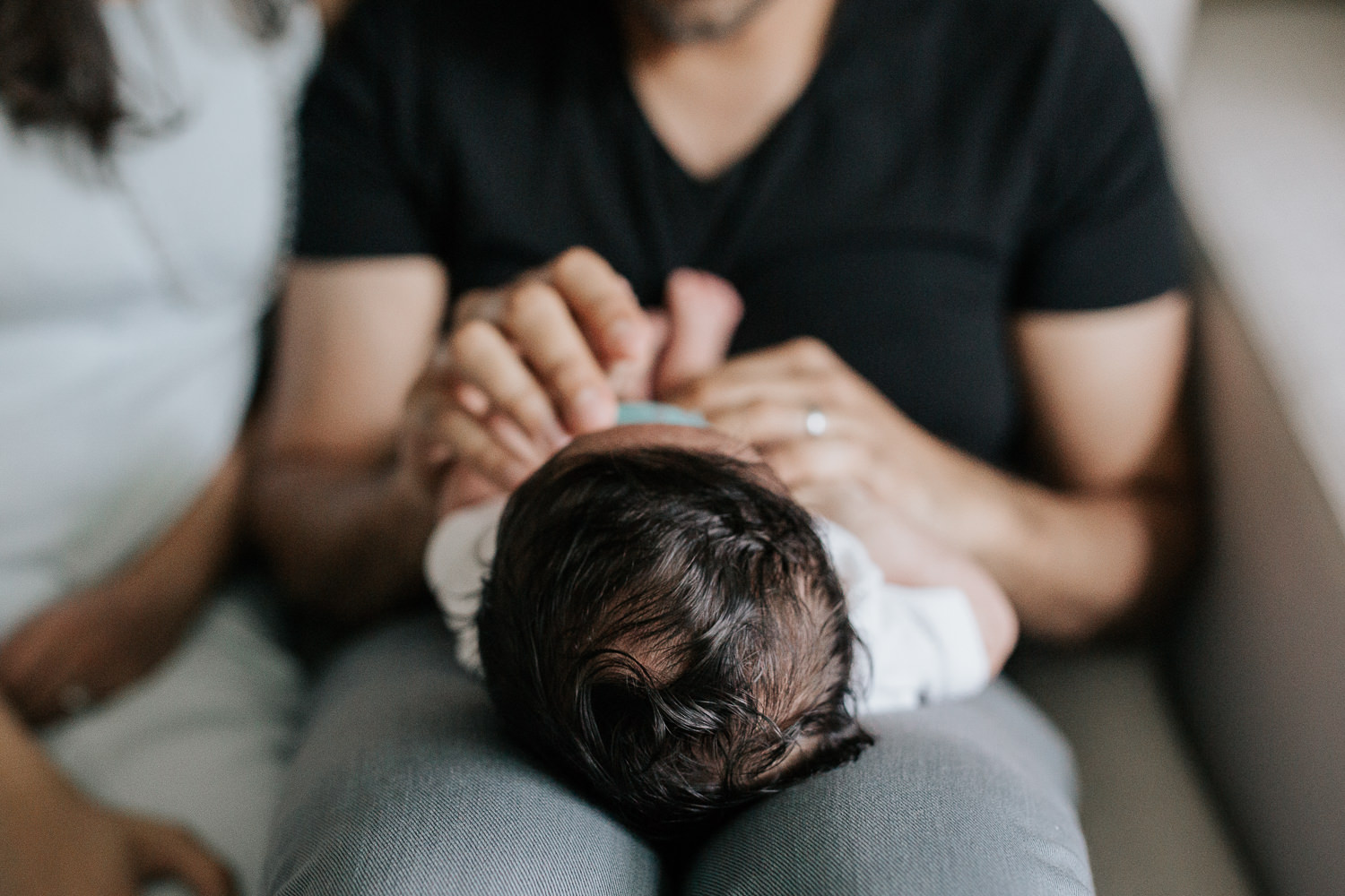 new parents sitting on couch, 1 month old baby boy in onesie with dark hair lying on dad's lap, close up of hair - Stouffville Lifestyle Photos