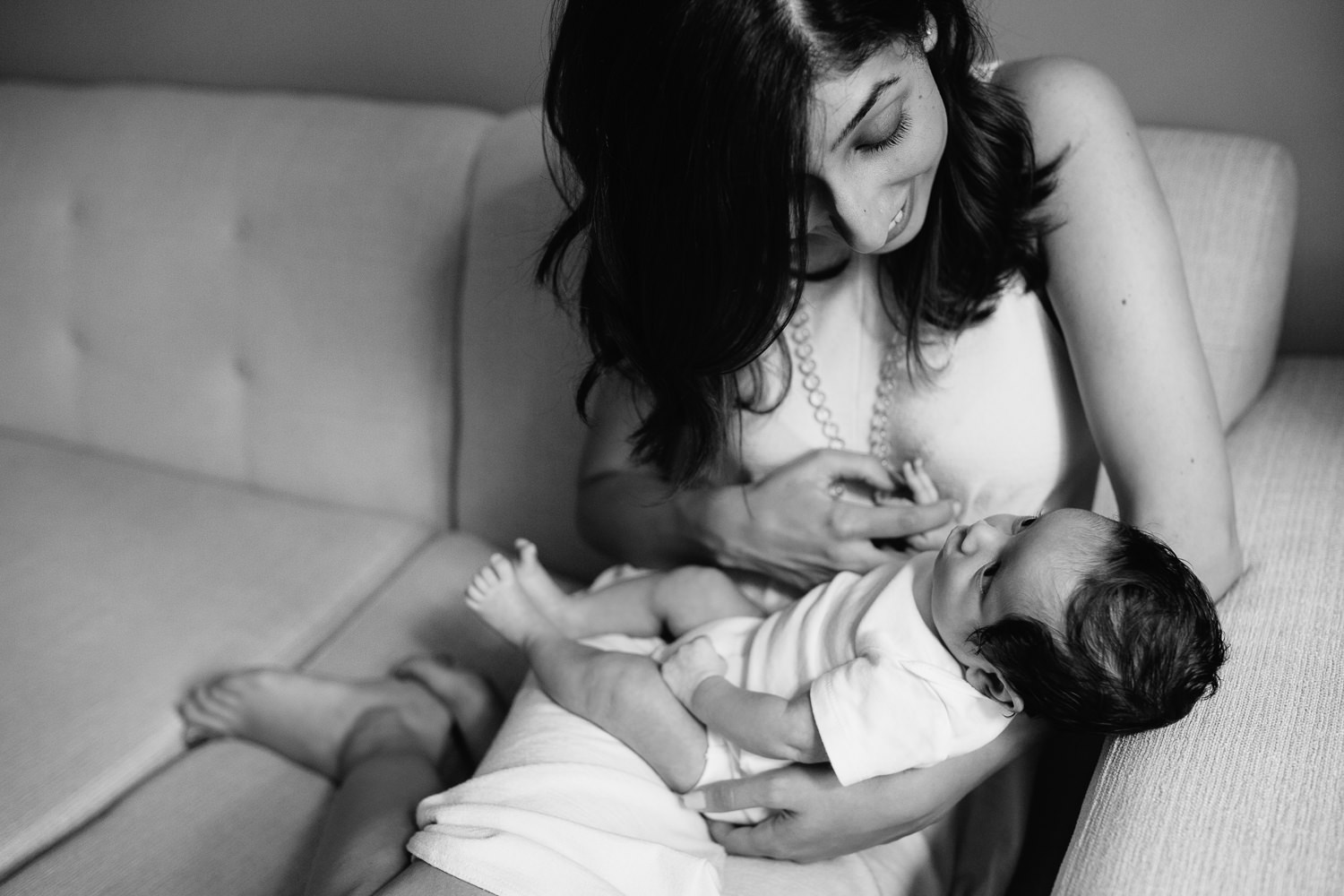 new mom sitting on couch snuggling 1 month old baby boy with dark hair in her arms - Newmarket Lifestyle Photography