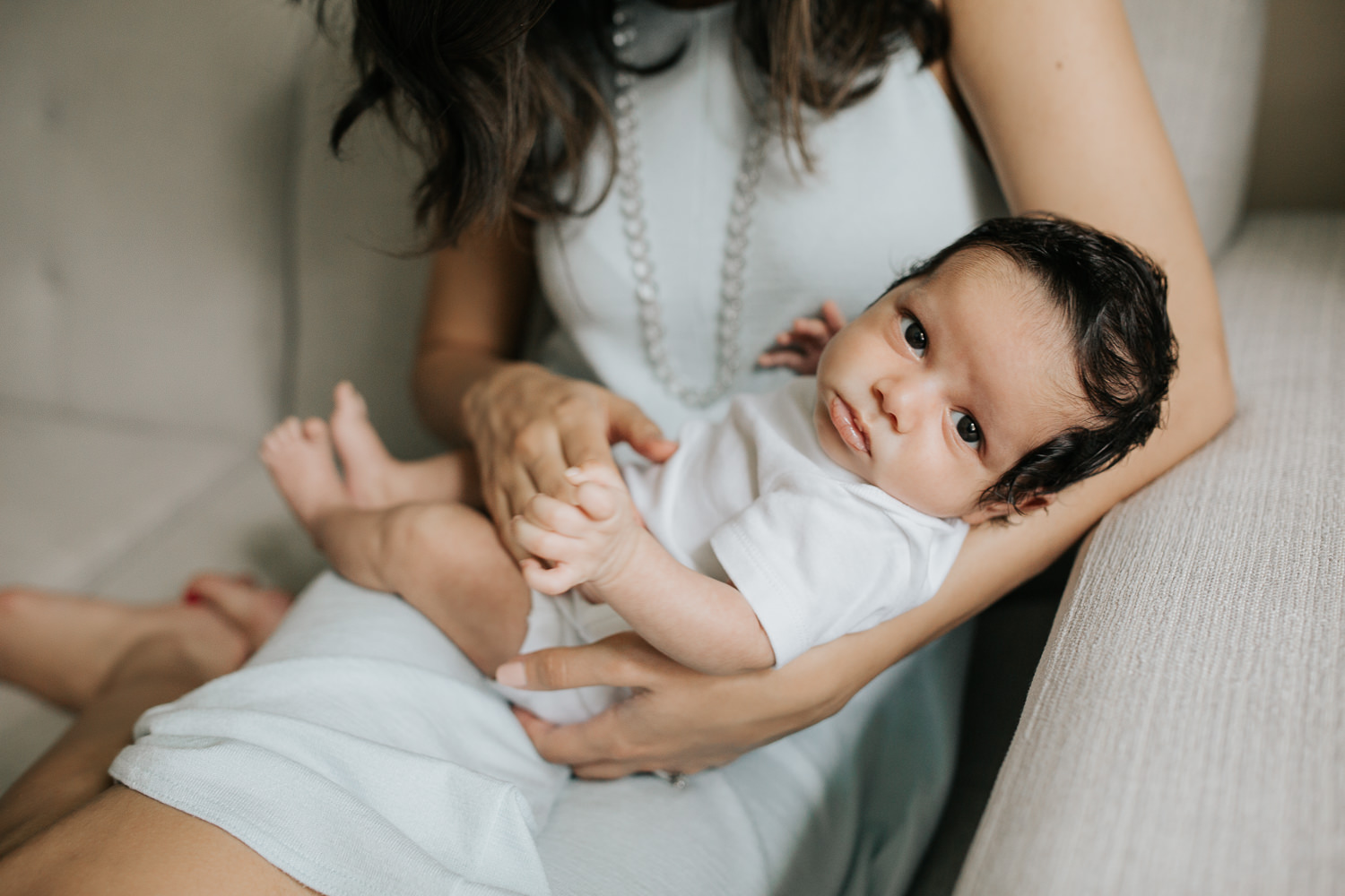 1 month old baby boy with dark hair wearing onesie lying in mom's arms and looking at camera - York Region Lifestyle Photos