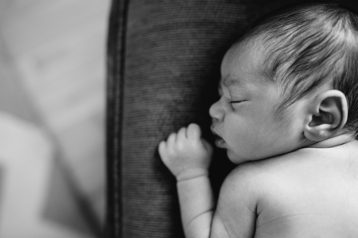 2 week old baby boy with dark hair sleeping on stomach on dark grey chair, close up of face - Newmarket In-Home Photos