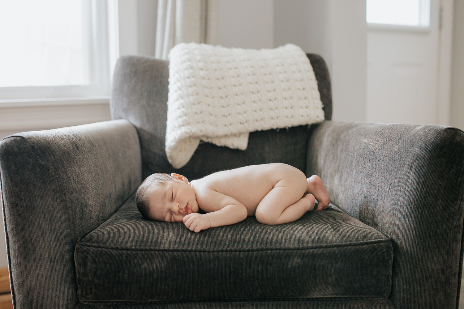 2 week old baby boy with dark hair sleeping on stomach on dark grey chair - York Region In-Home Photography