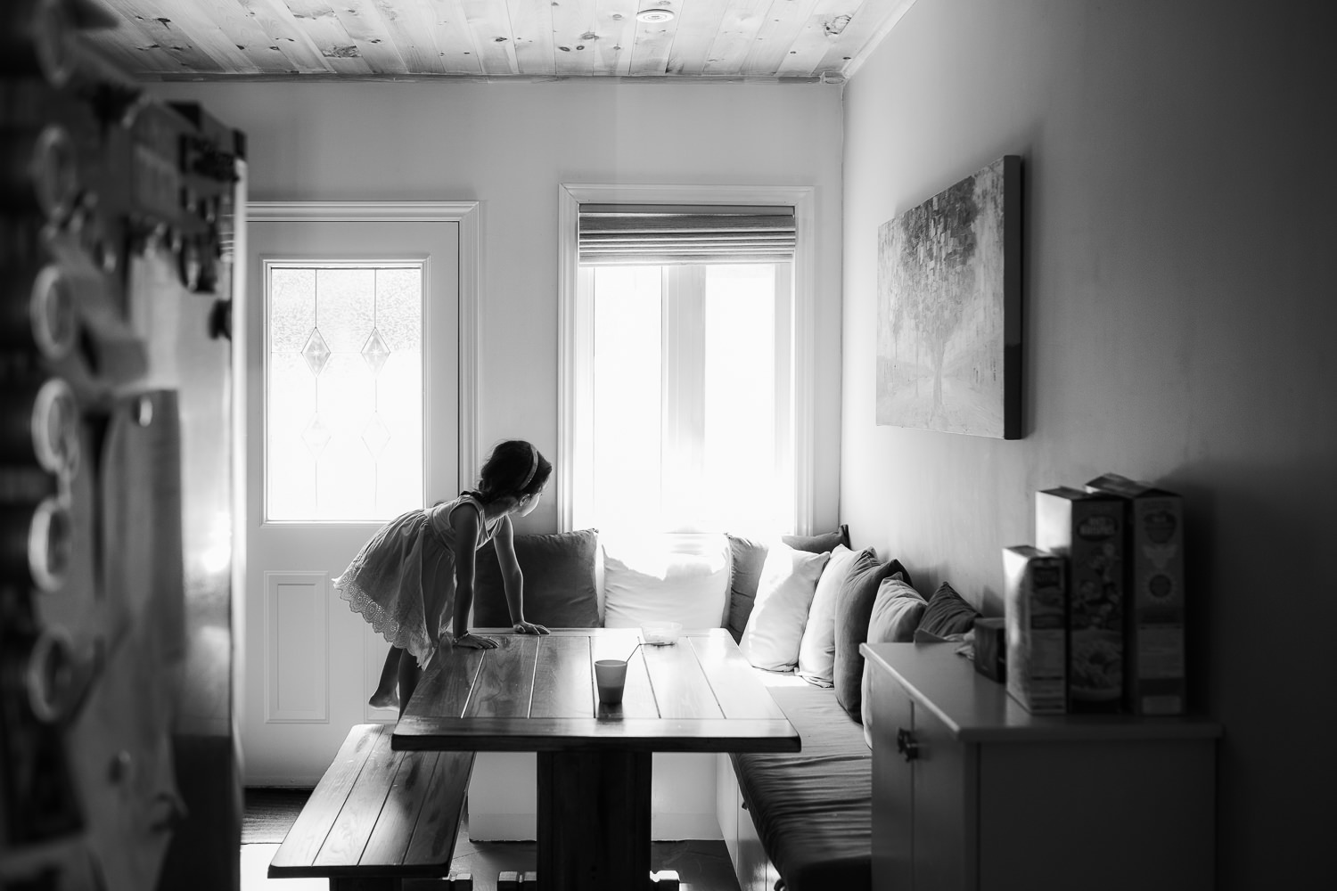 4 year old toddler girl with dark hair in pigtails wearing purple dress climbing on kitchen table bench and looking out window - GTA In-Home Photos