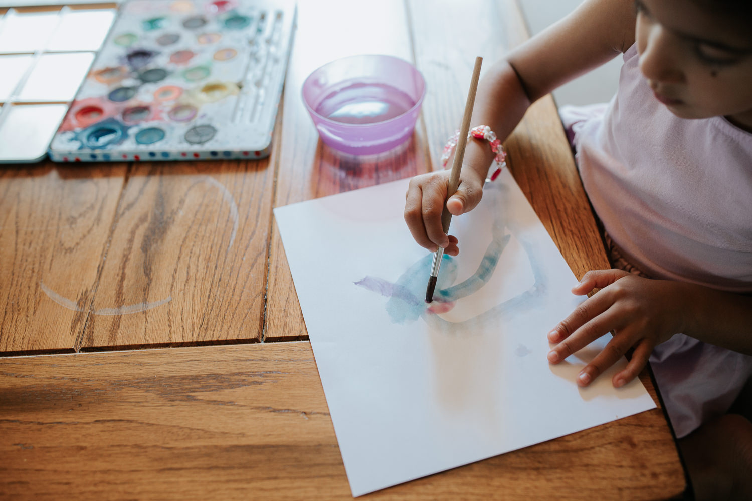 4 year old toddler girl with dark hair in pigtails wearing purple dress sitting at kitchen table painting with watercolours - Stouffville Lifestyle Photos
