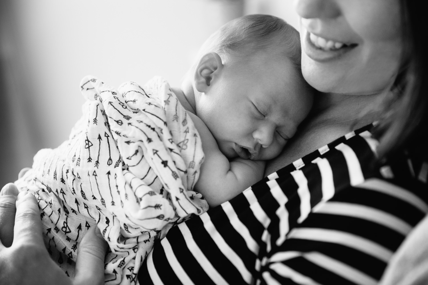 2 week old baby girl with light hair wrapped in black and white arrow swaddle sleeping on mother's chest as mom reclines in bed - GTA Lifestyle Photography