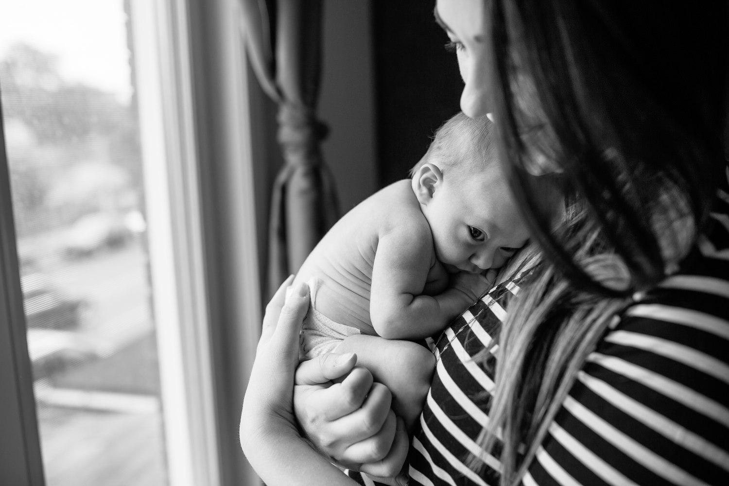 2 week old baby girl with light hair in diaper lying on mom's chest wide awake and calm as mother snuggles daughter - Barrie In-Home Photography