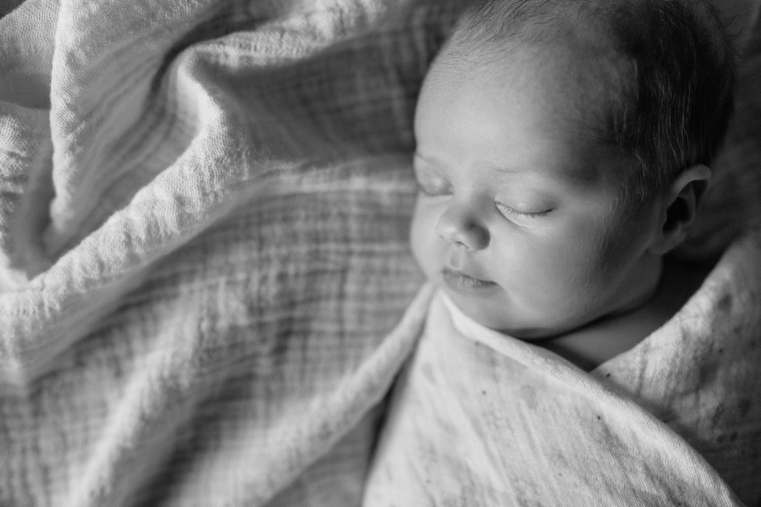 2 week old baby girl with light hair lying on bed wrapped in swaddle, asleep with soft smile on her lips - Newmarket In-Home Photos
