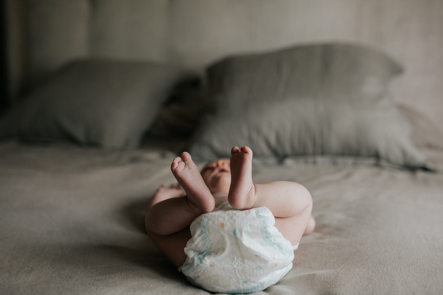 2 week old baby girl in diaper lying on master bed, feet in air - Markham In-Home Photos