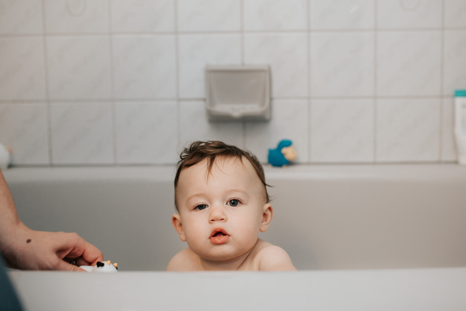 9 month old baby boy with dark hair and blue eyes sitting in bathtub looking at camera - Barrie Golden Hour Photos