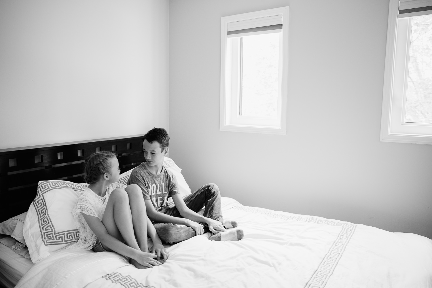11 year old girl and 13 year old boy sitting on white bed, brother and sister looking at each other - Stouffville In-Home Photography