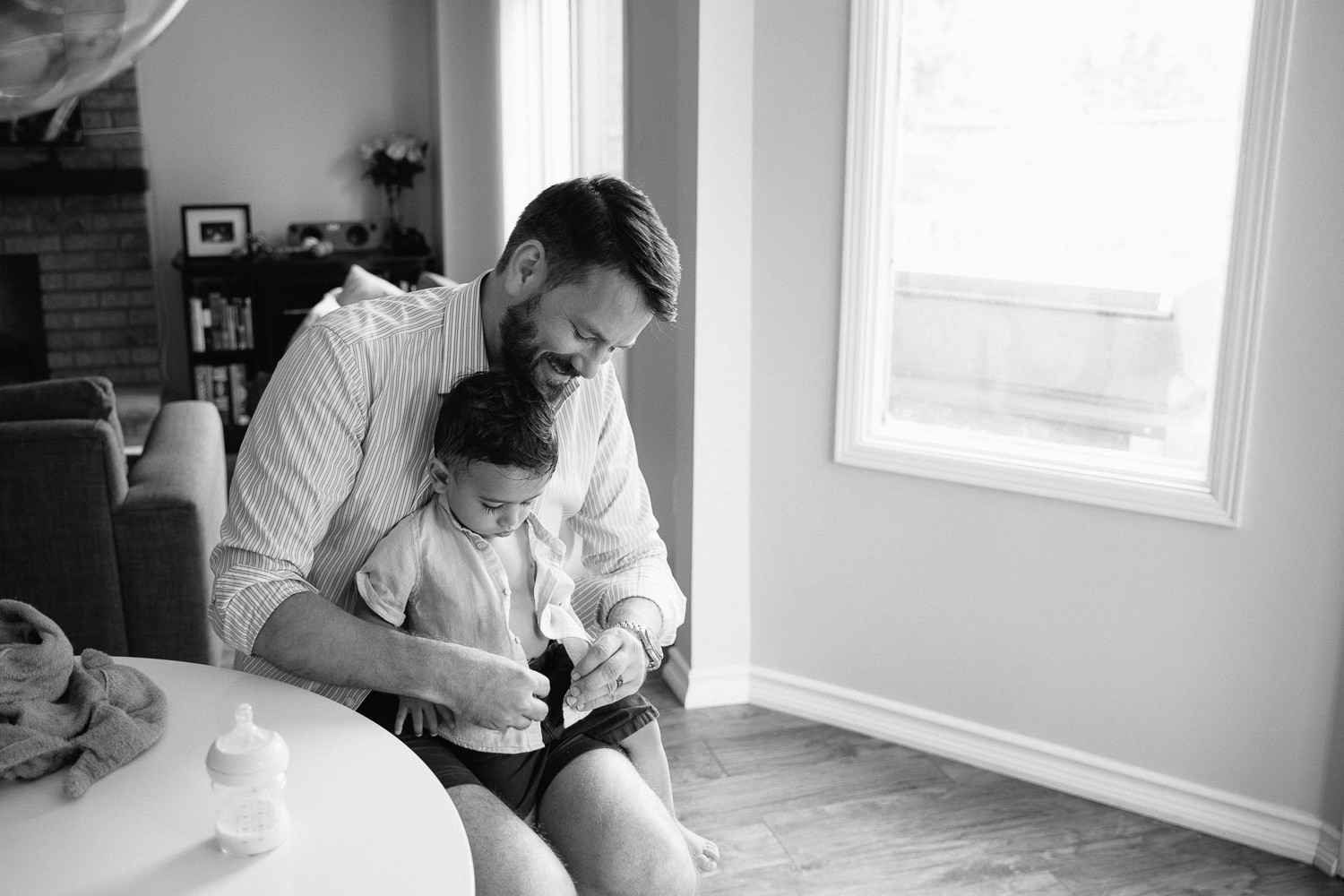 1 year old baby boy with dark hair and long eyelashes sitting in dad's lap as father button's son's shirt - GTA In-Home Photos