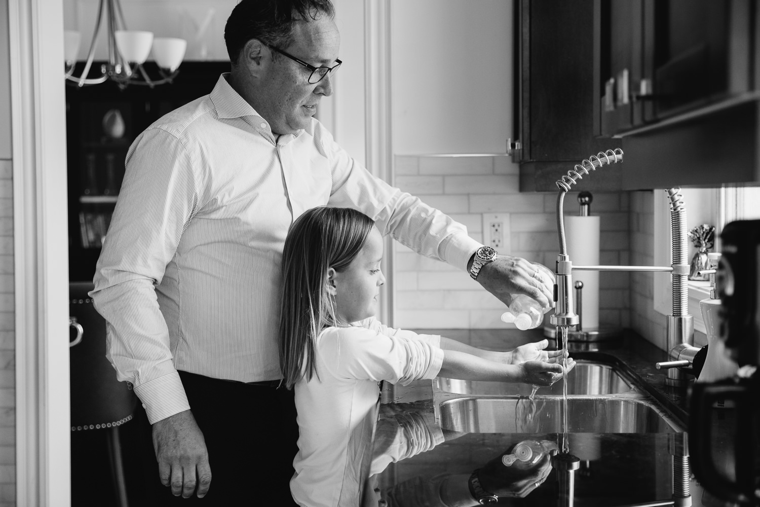 father and 8 year old daughter standing at kitchen sink, dad pouring dish soap into girl's outstretched hands - Markham In-Home Photos