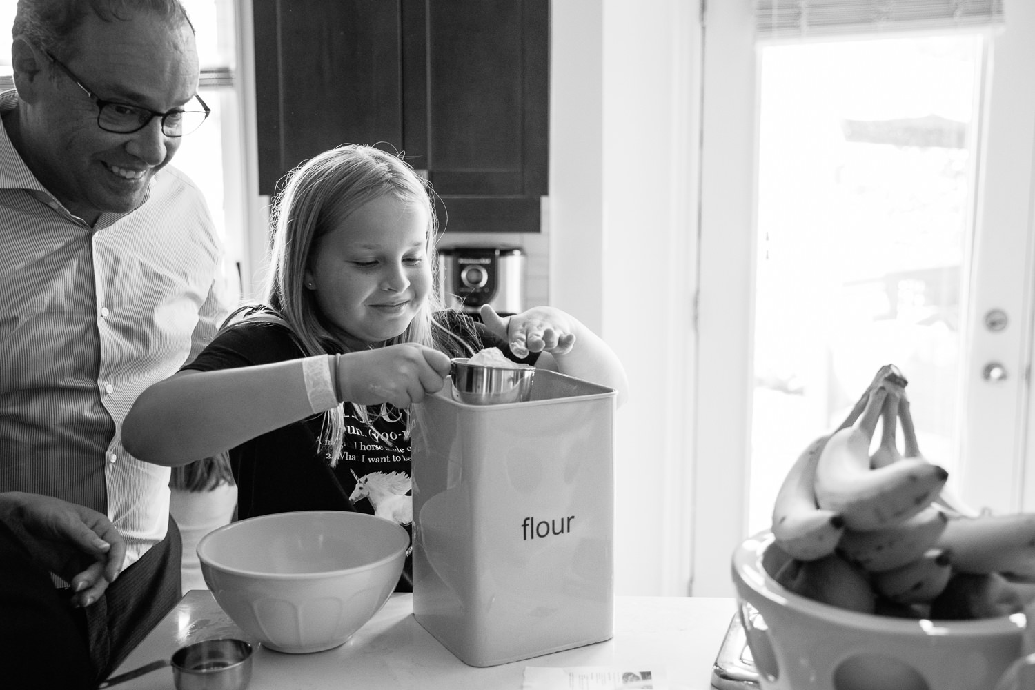 father leaning over 10 year old daughter's shoulder as she measures flour to make pancakes for family brunch - Stouffville Lifestyle Photos