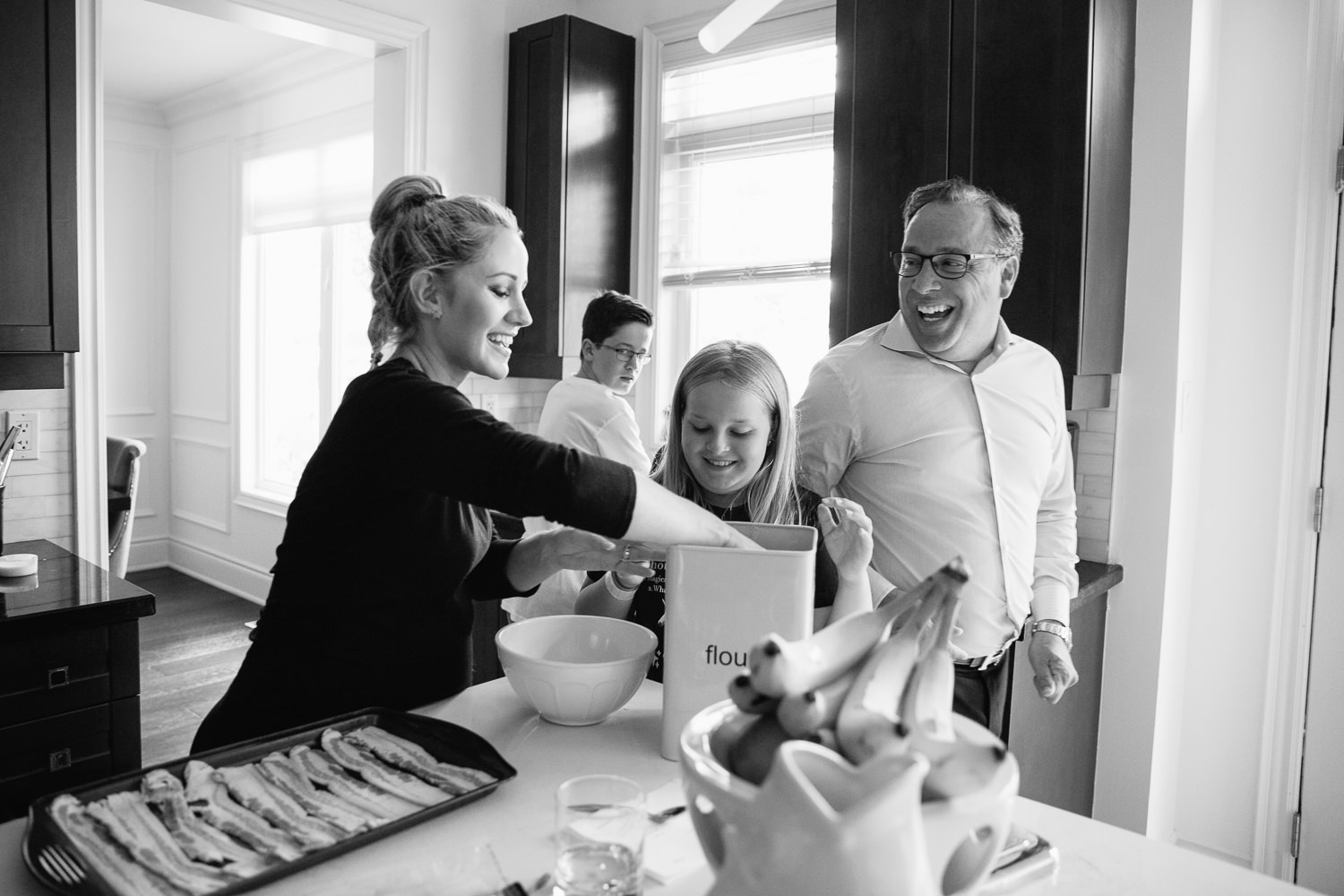 family laughing together in kitchen, mom and 10 year old daughter scooping flour as dad walks by, 13 year old boy in background - Barrie Lifestyle Photos