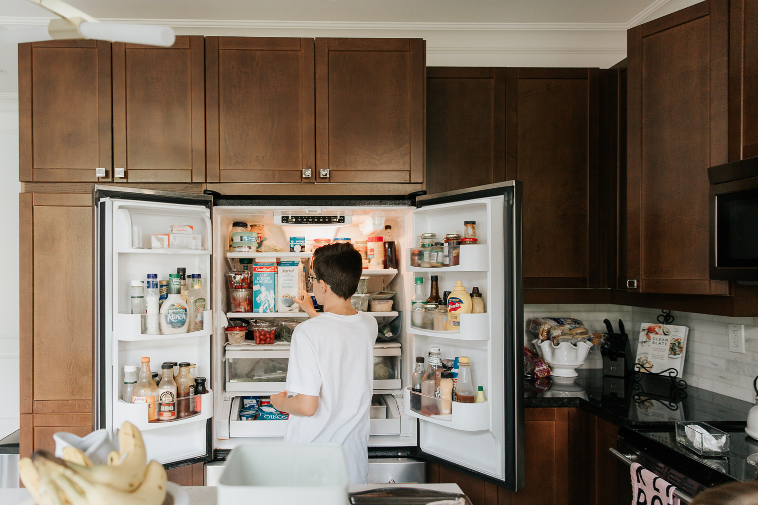 13 year old boy standing in front of open fridge looking for milk as he helps prepare family brunch - Markham Lifestyle Photos